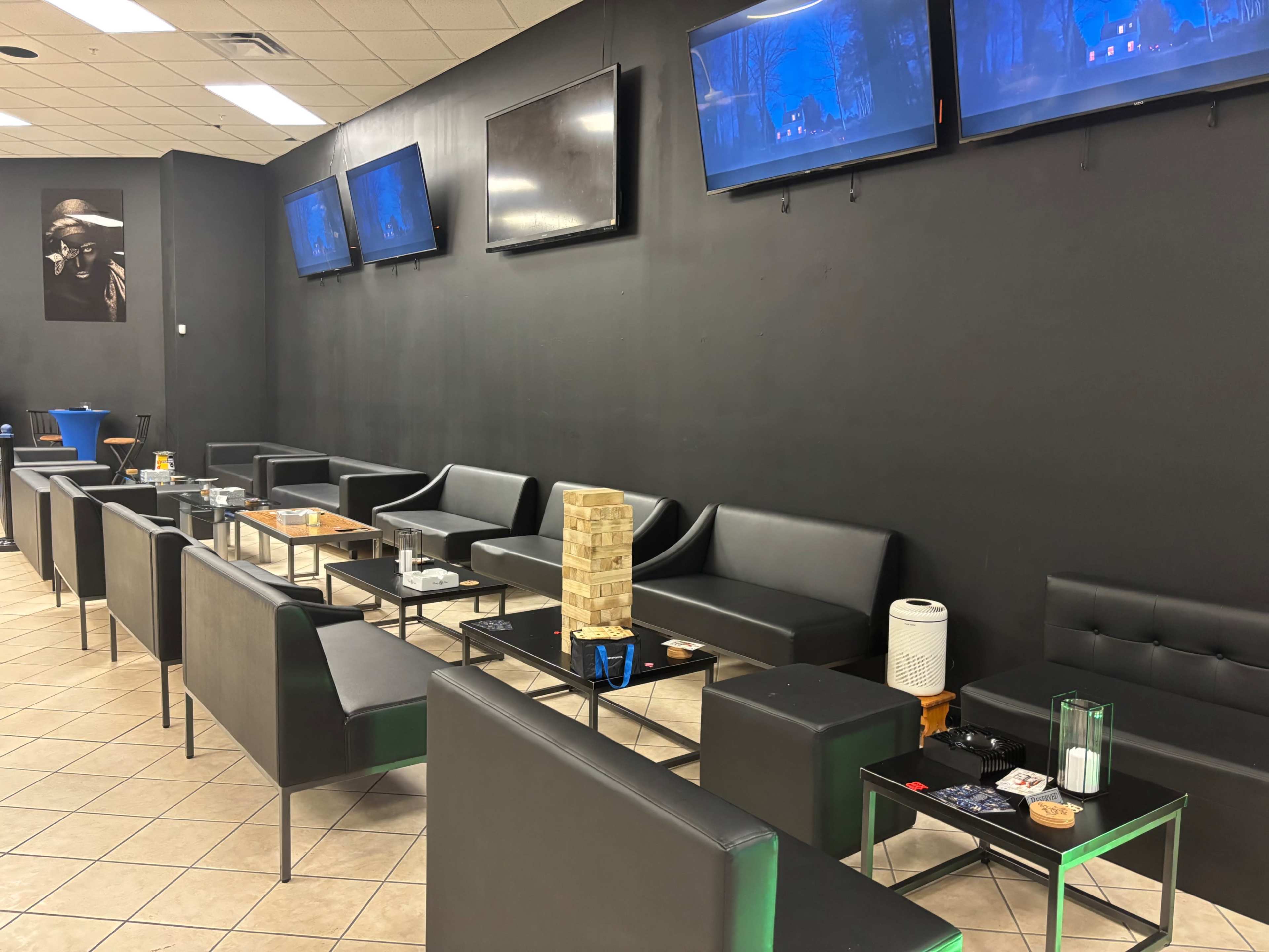 The scene shows a modern lounge area with black walls, several flat-screen TVs mounted, and multiple black seating arrangements around glass tables.