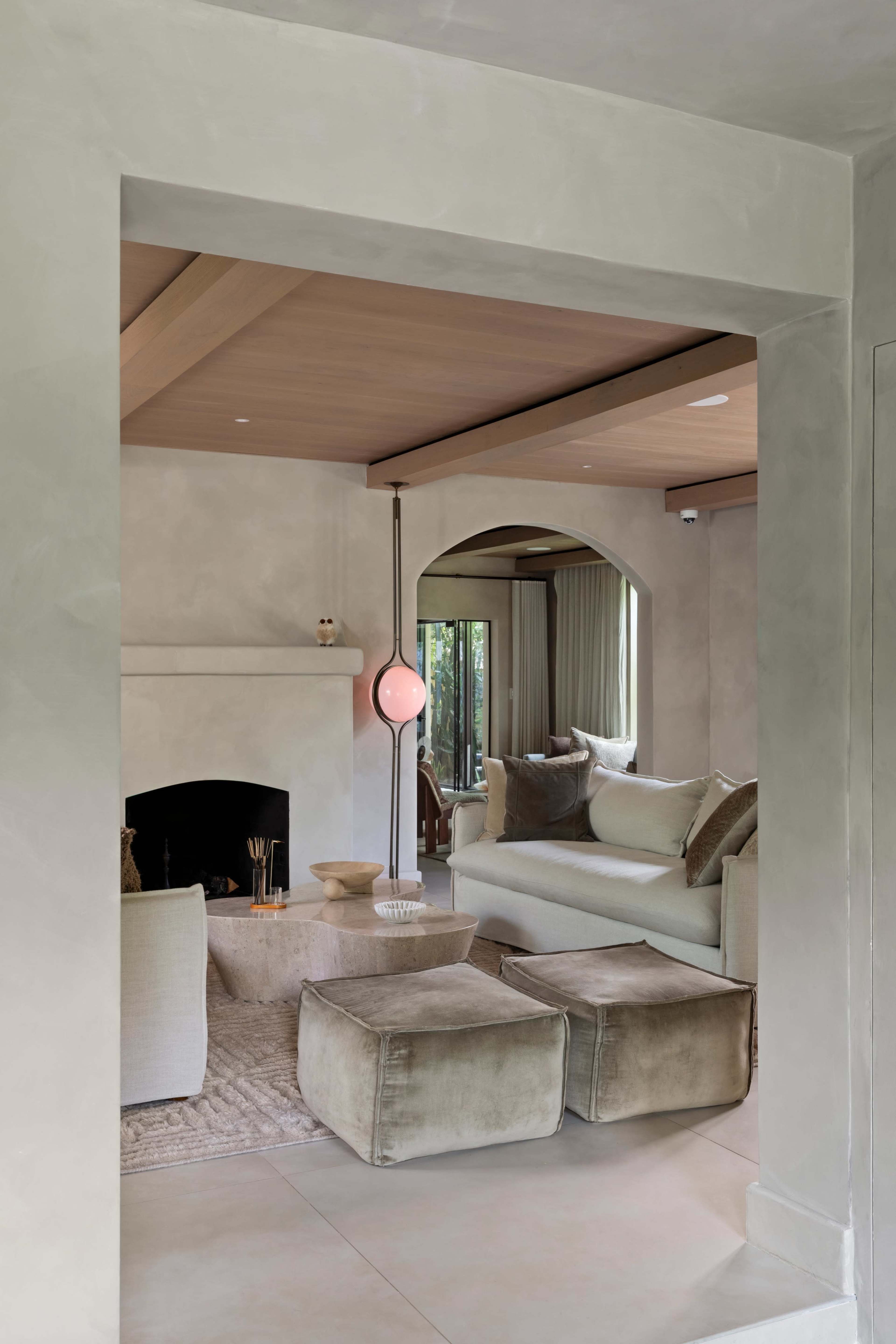 A modern living room features a cozy seating area with a light-colored sofa and a fireplace, framed by an archway with a pendant light hanging above.