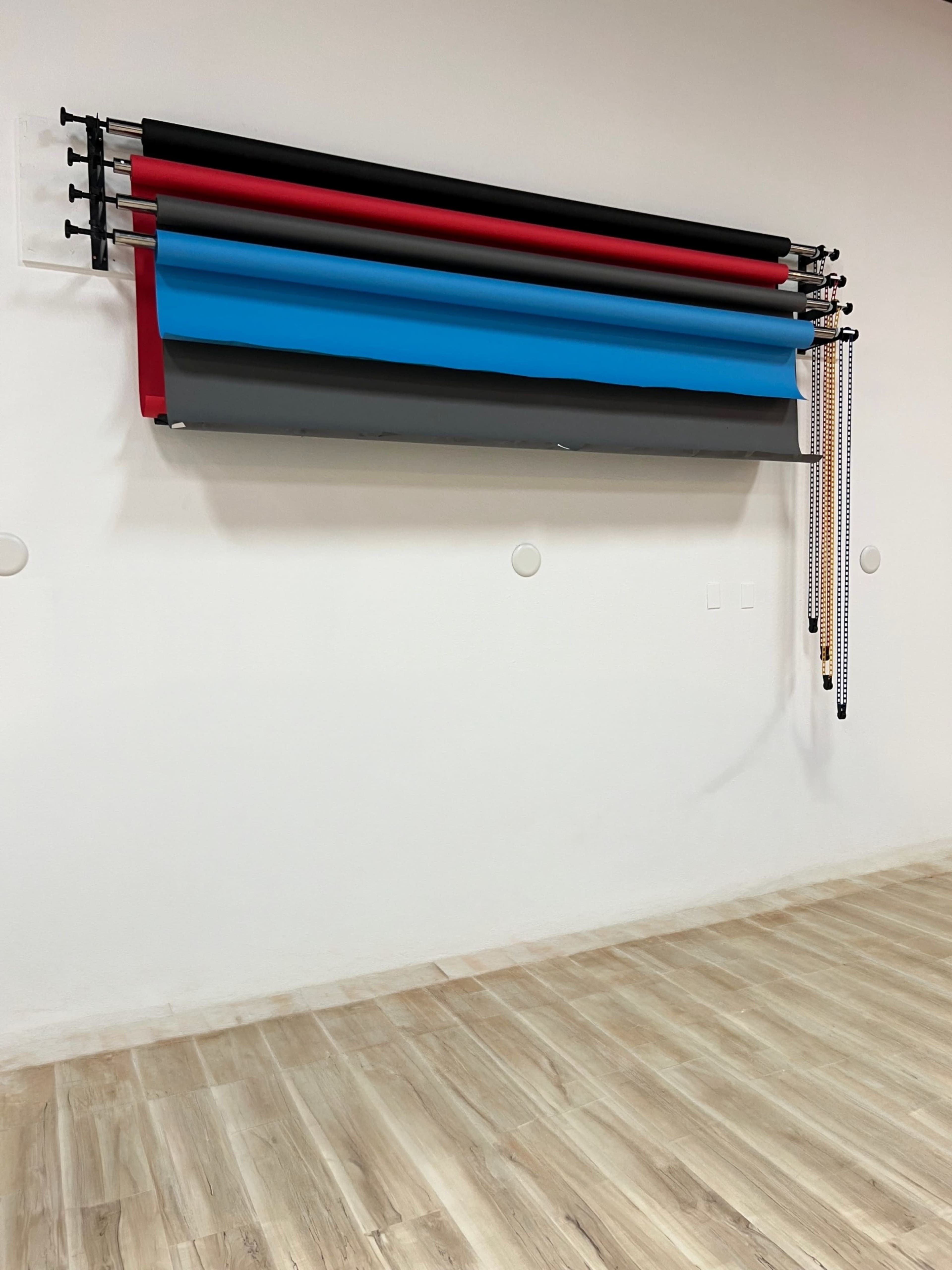 A series of colored backdrop rolls is mounted on a wall in a room with wooden flooring.