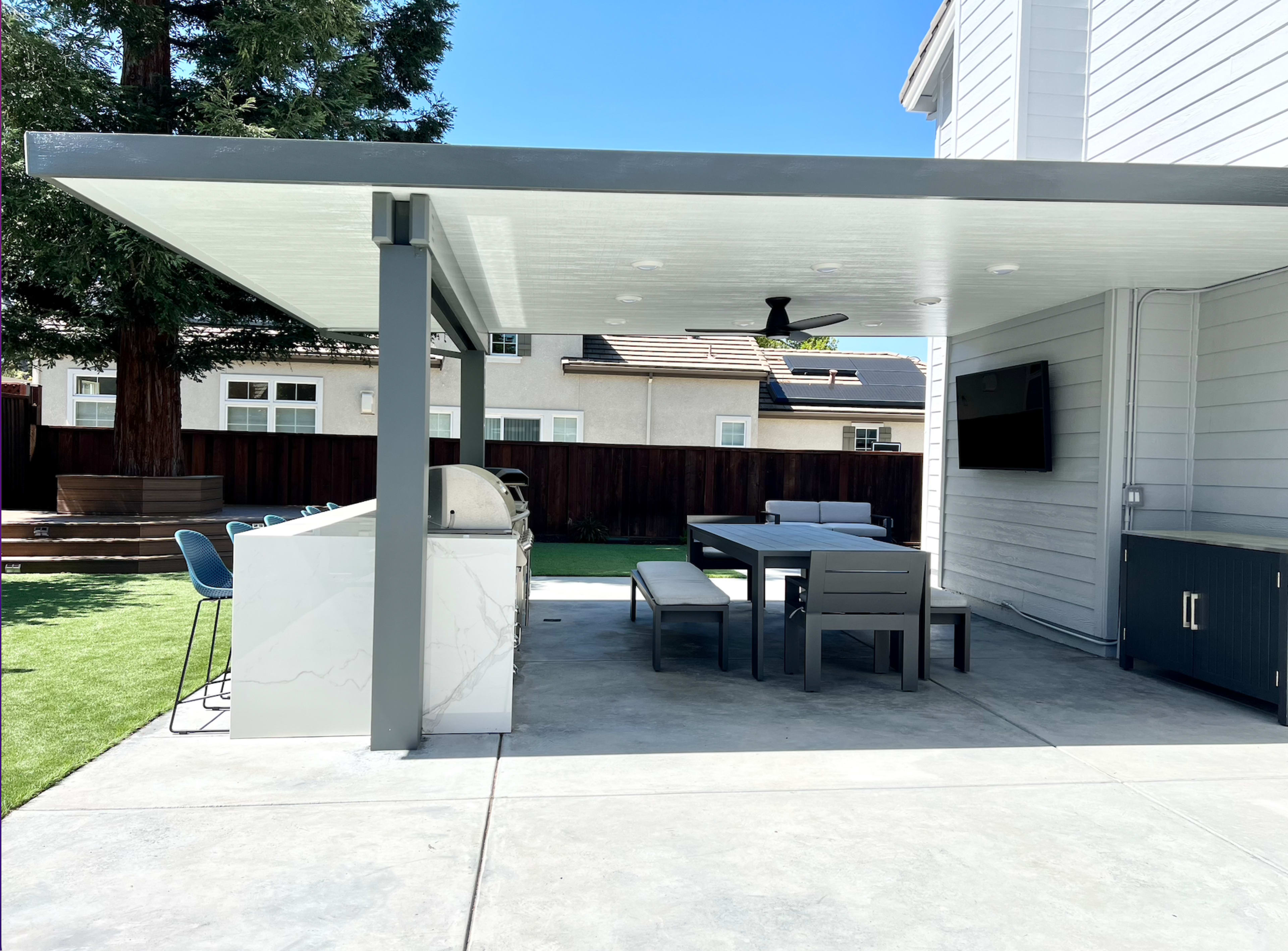 A modern outdoor kitchen and dining area with a covered patio, featuring a barbecue grill, table, and seating.