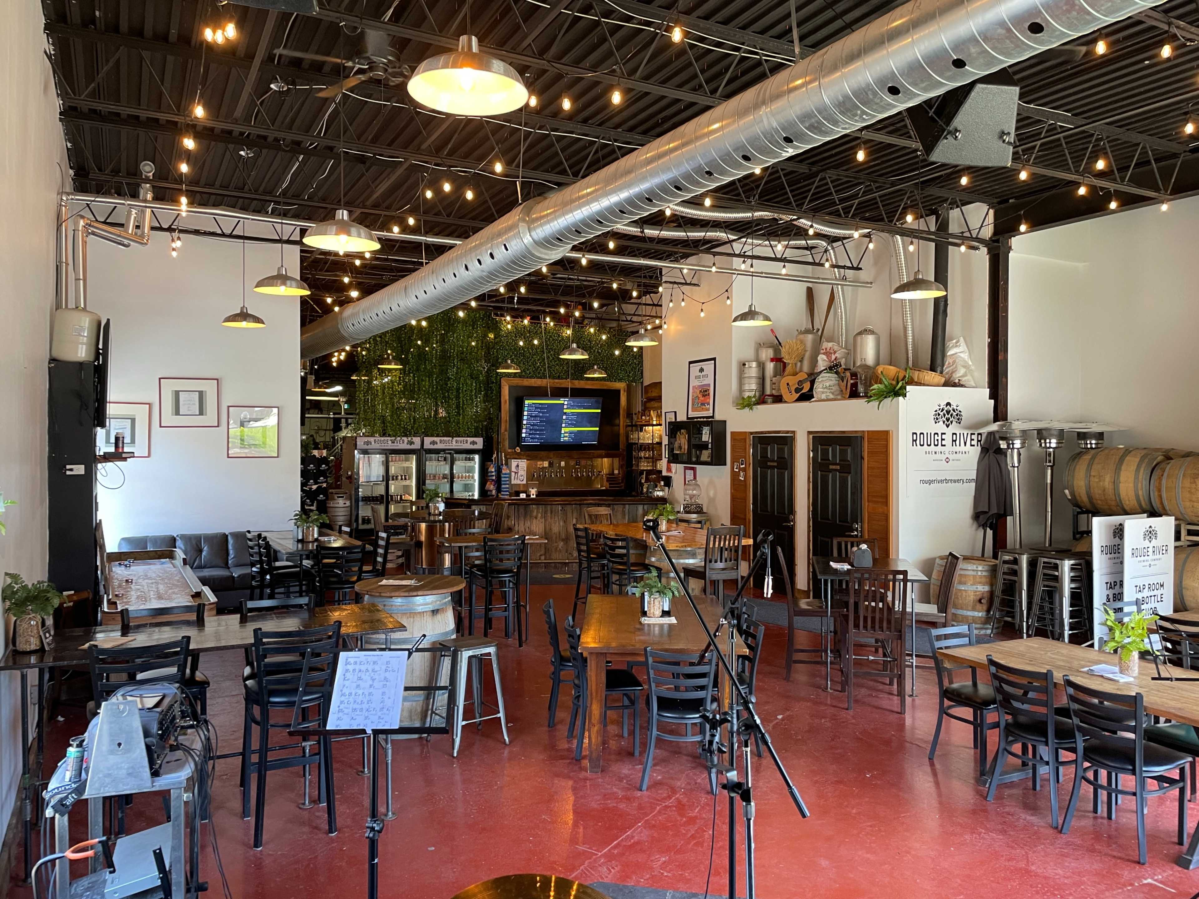 A spacious restaurant interior with wooden tables, chairs, a bar area, and hanging lights.