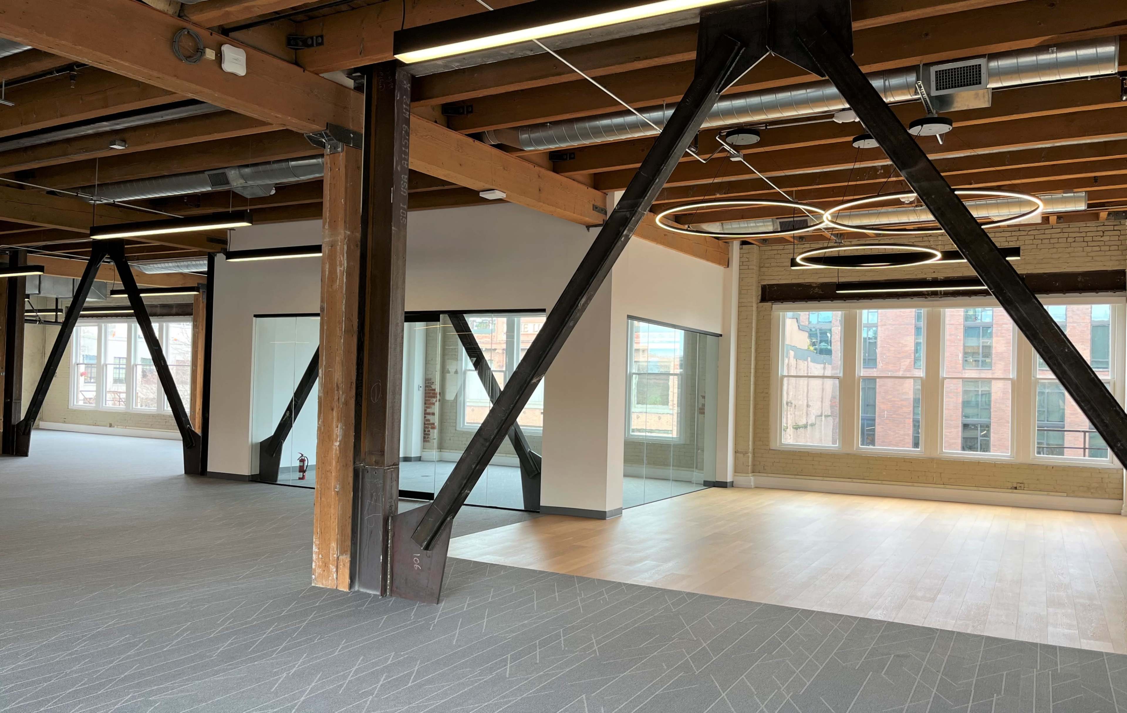 The image shows an open office space with exposed wooden beams, large windows, and a glass-walled meeting room.