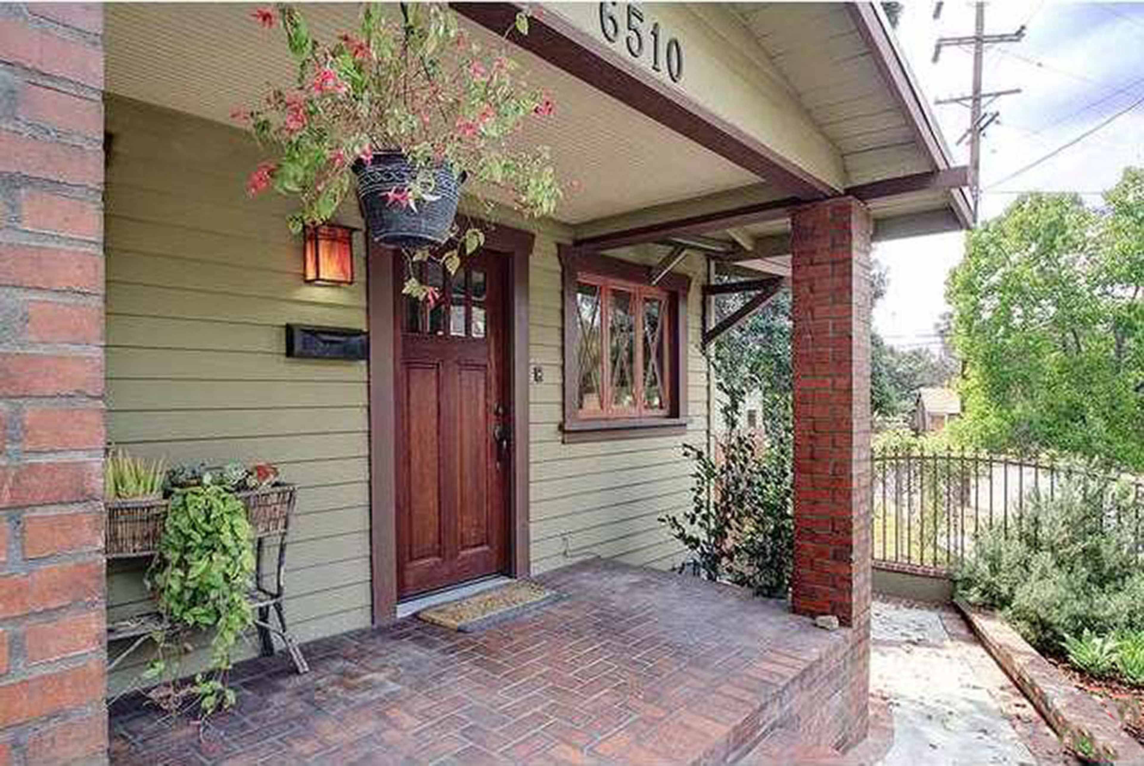 The entrance of a house with a wooden front door, brick accents, and potted plants on the porch.