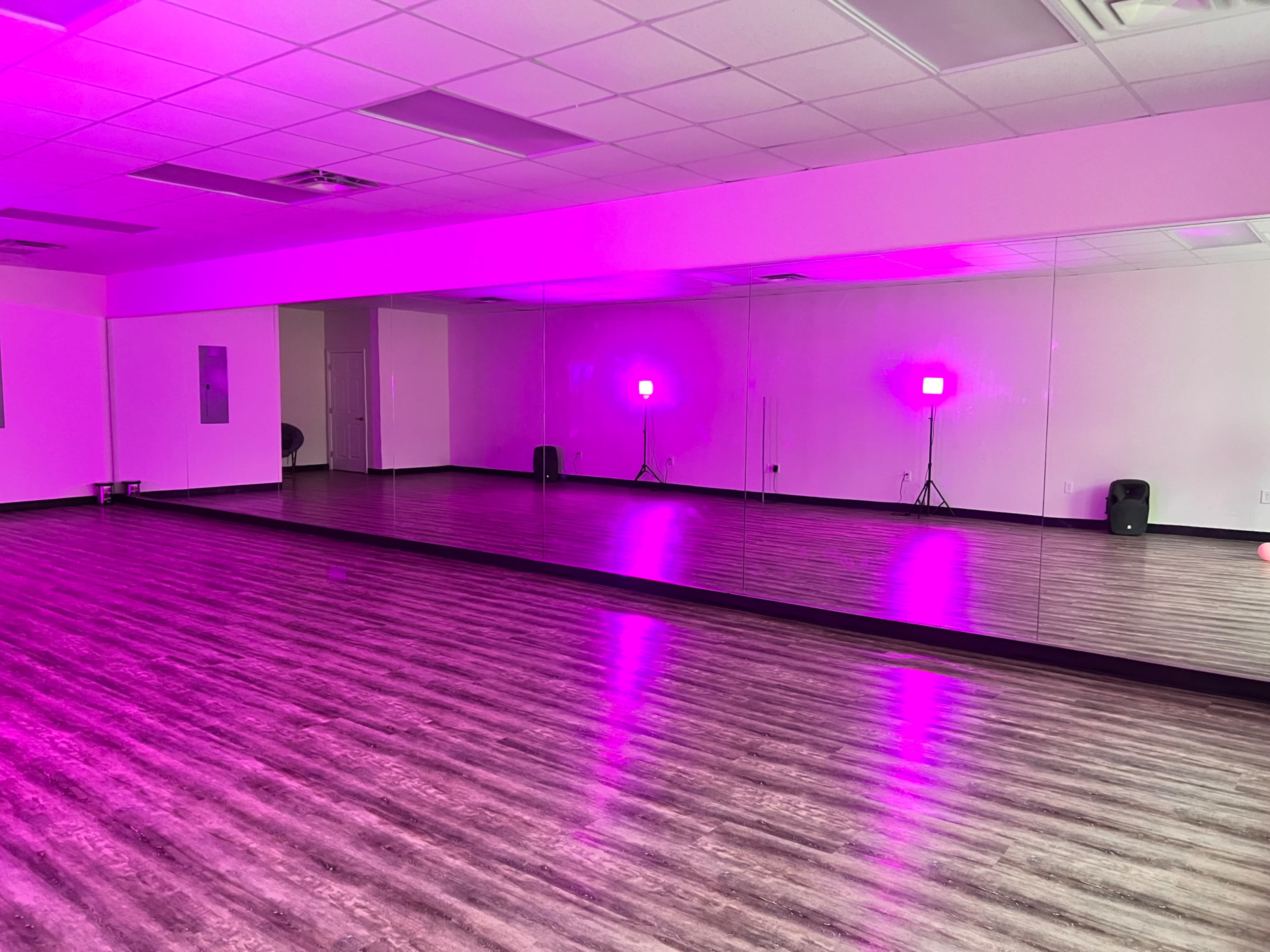 A spacious dance studio with mirrored walls and pink lighting.