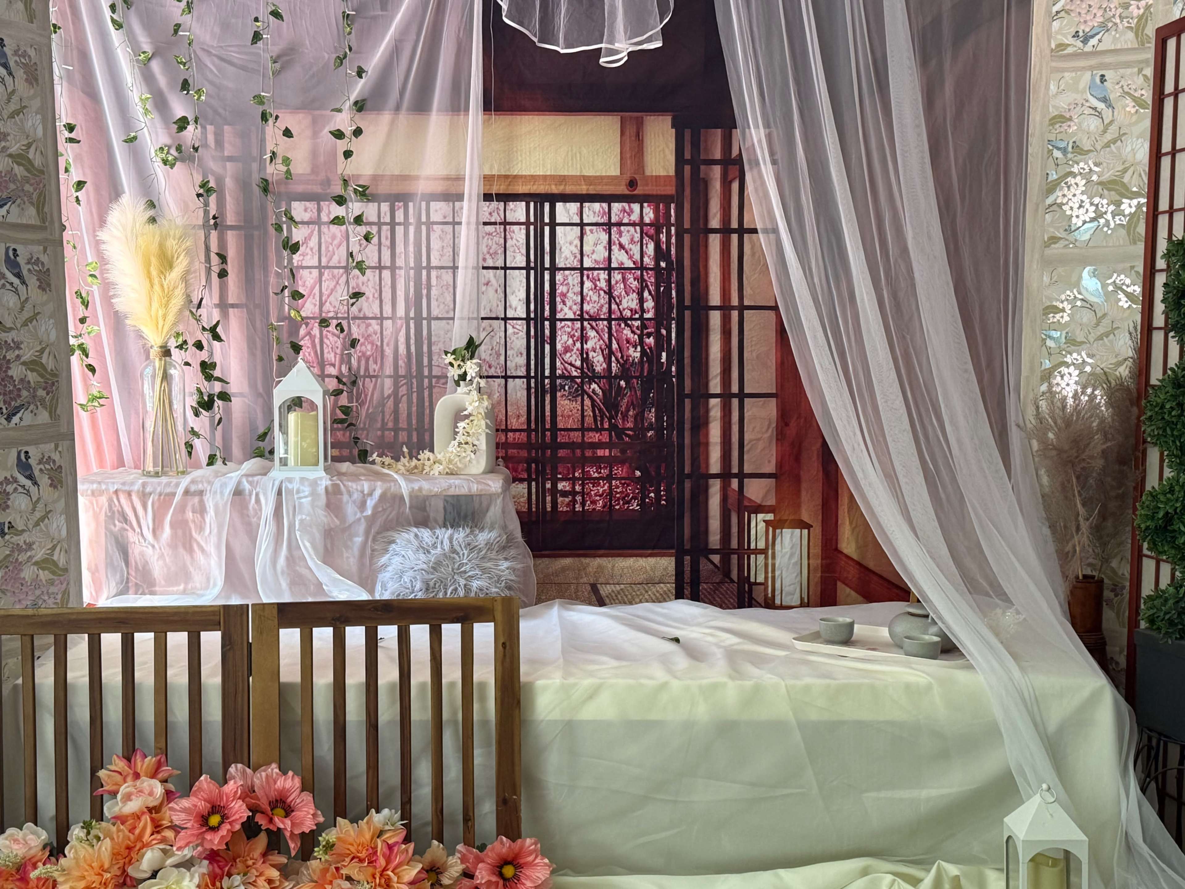 The scene features a decorative indoor space with a bed covered in white linens, surrounded by floral arrangements and sheer curtains, and a backdrop of a traditional Japanese-style room.