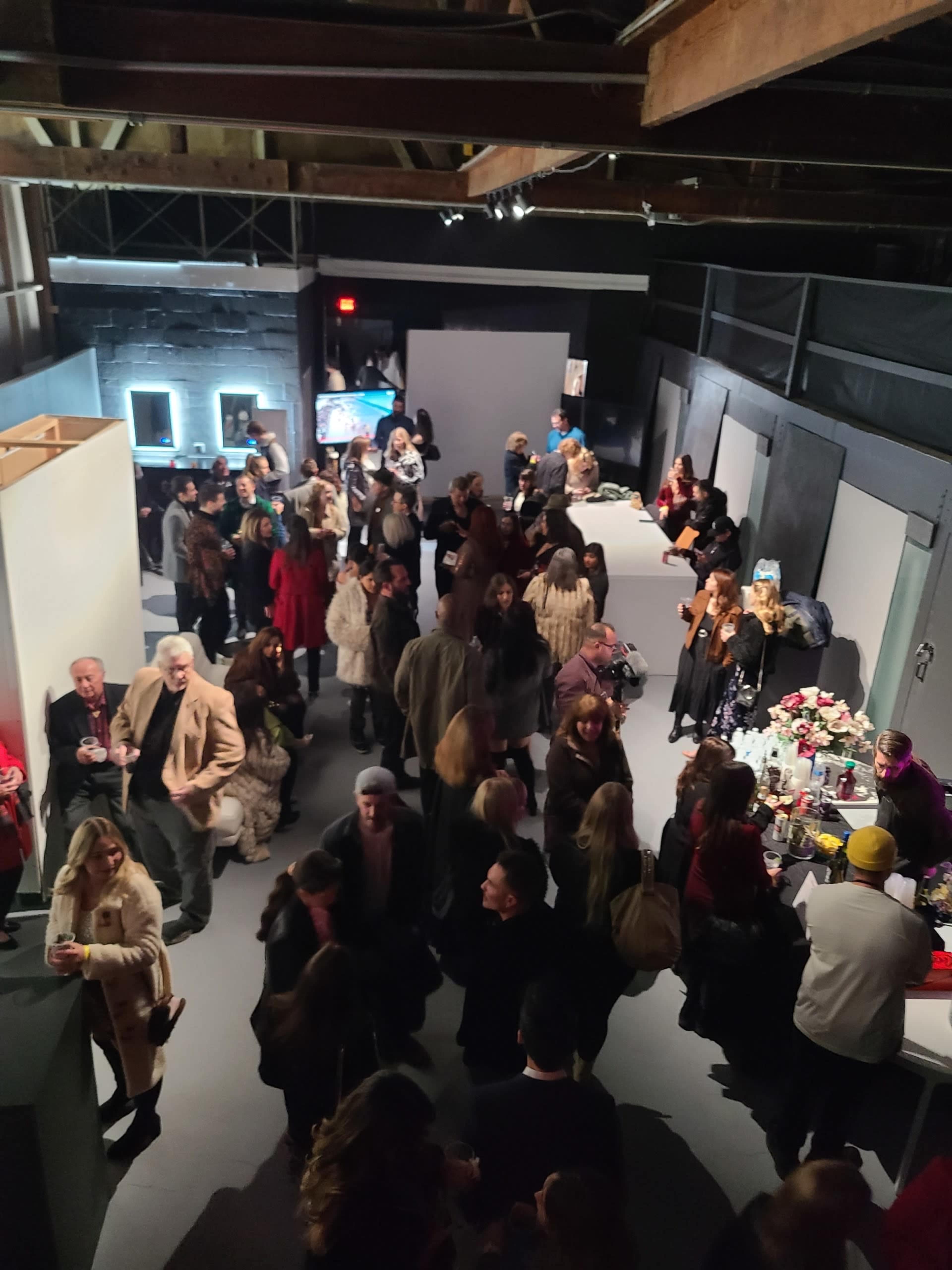 A large crowd of people socializes at an indoor event space featuring tables and artworks.
