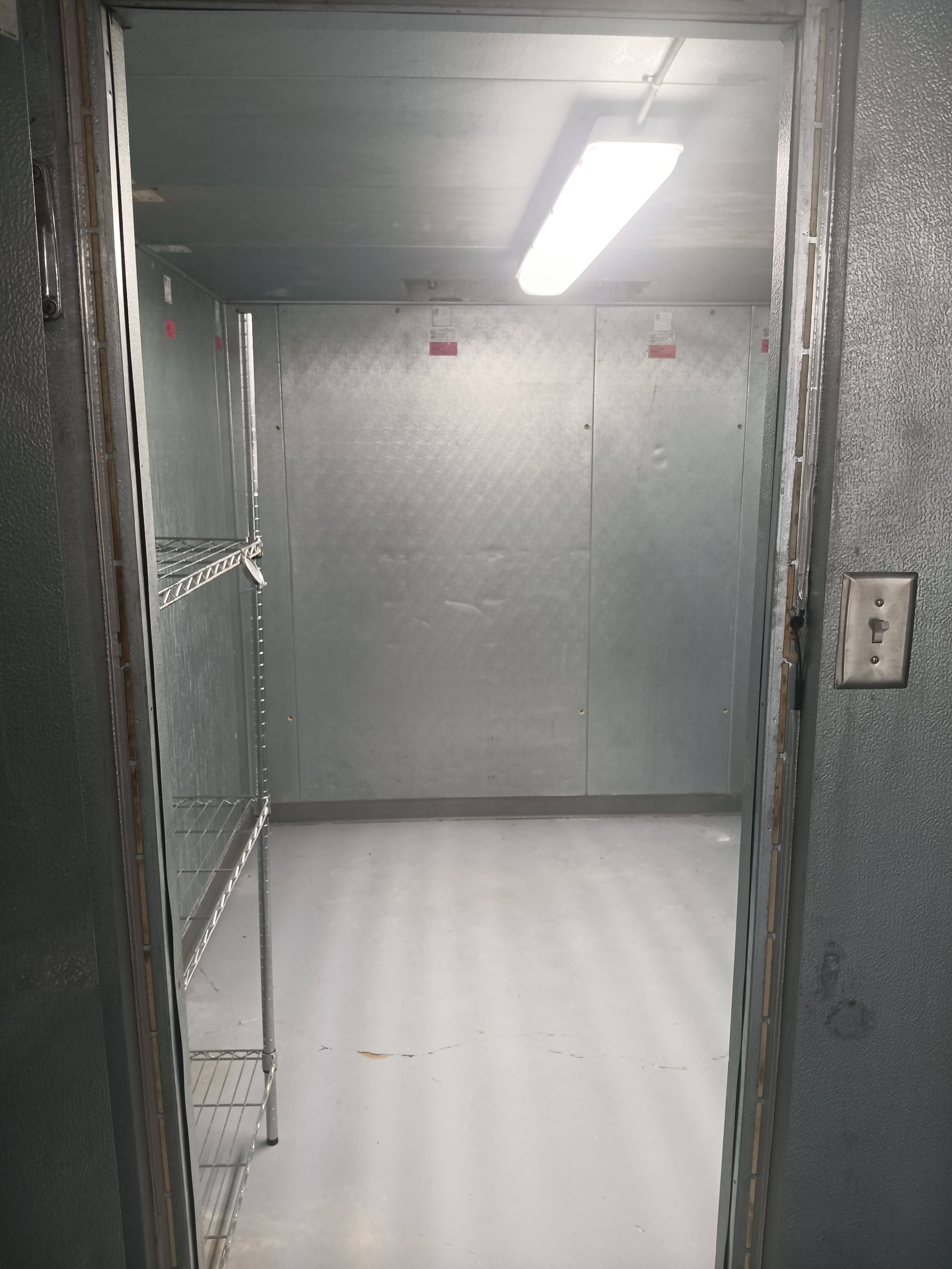 The image shows an empty storage room with metal shelving and gray walls, illuminated by fluorescent lighting.