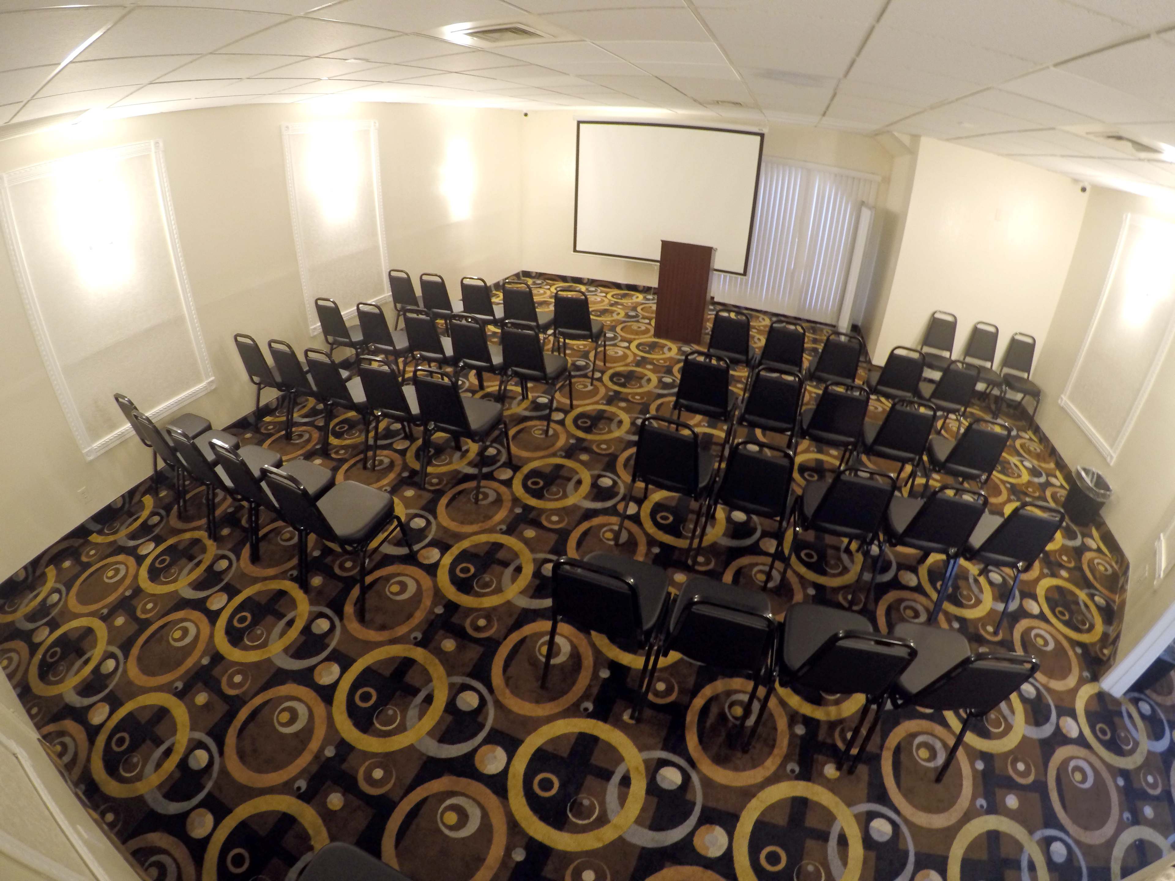 A meeting room is set up with rows of black chairs facing a presentation screen and a podium.