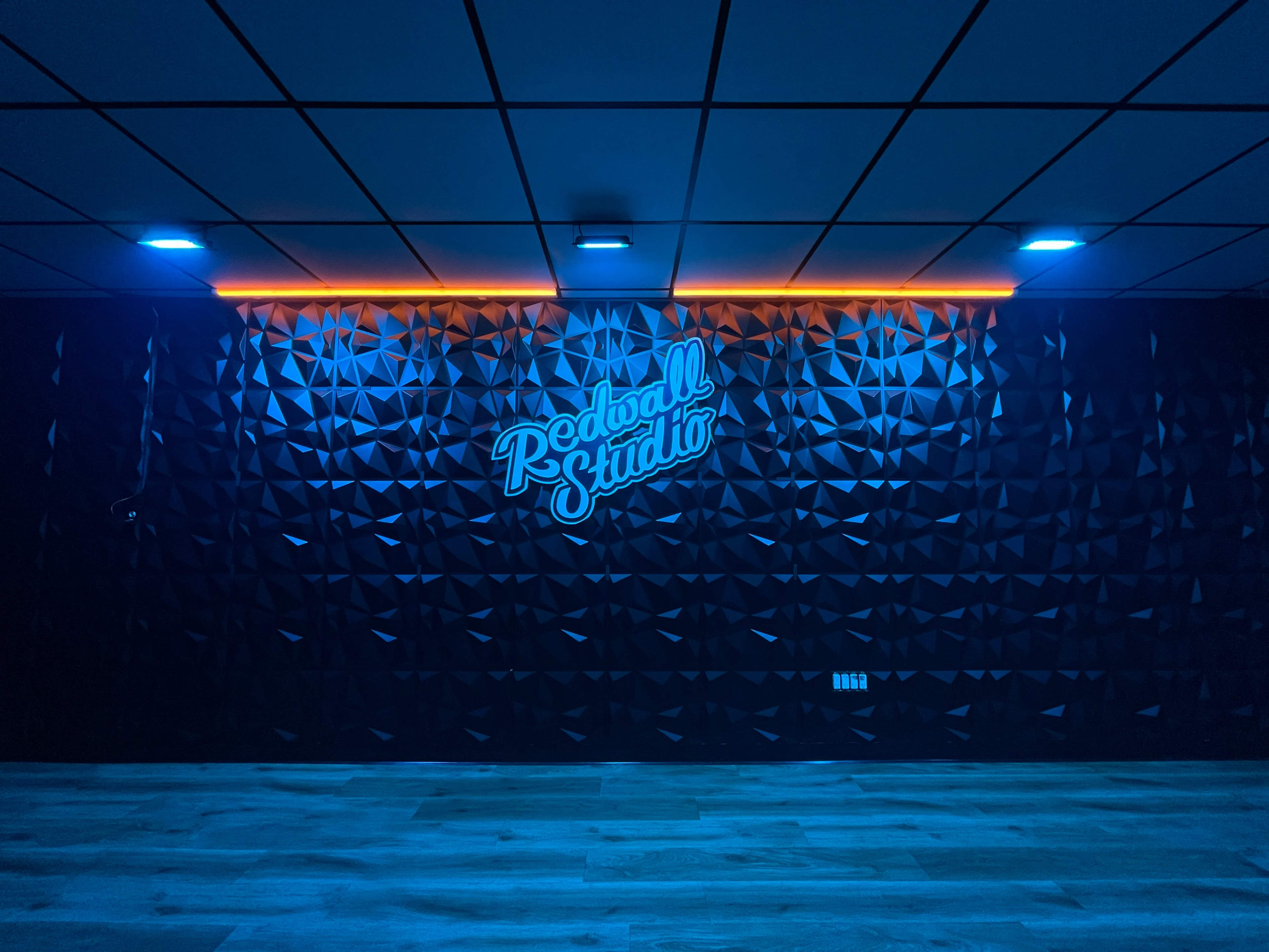 A studio interior with a 3D geometric wall design illuminated by blue and orange lights, featuring the text "Redball Studio."