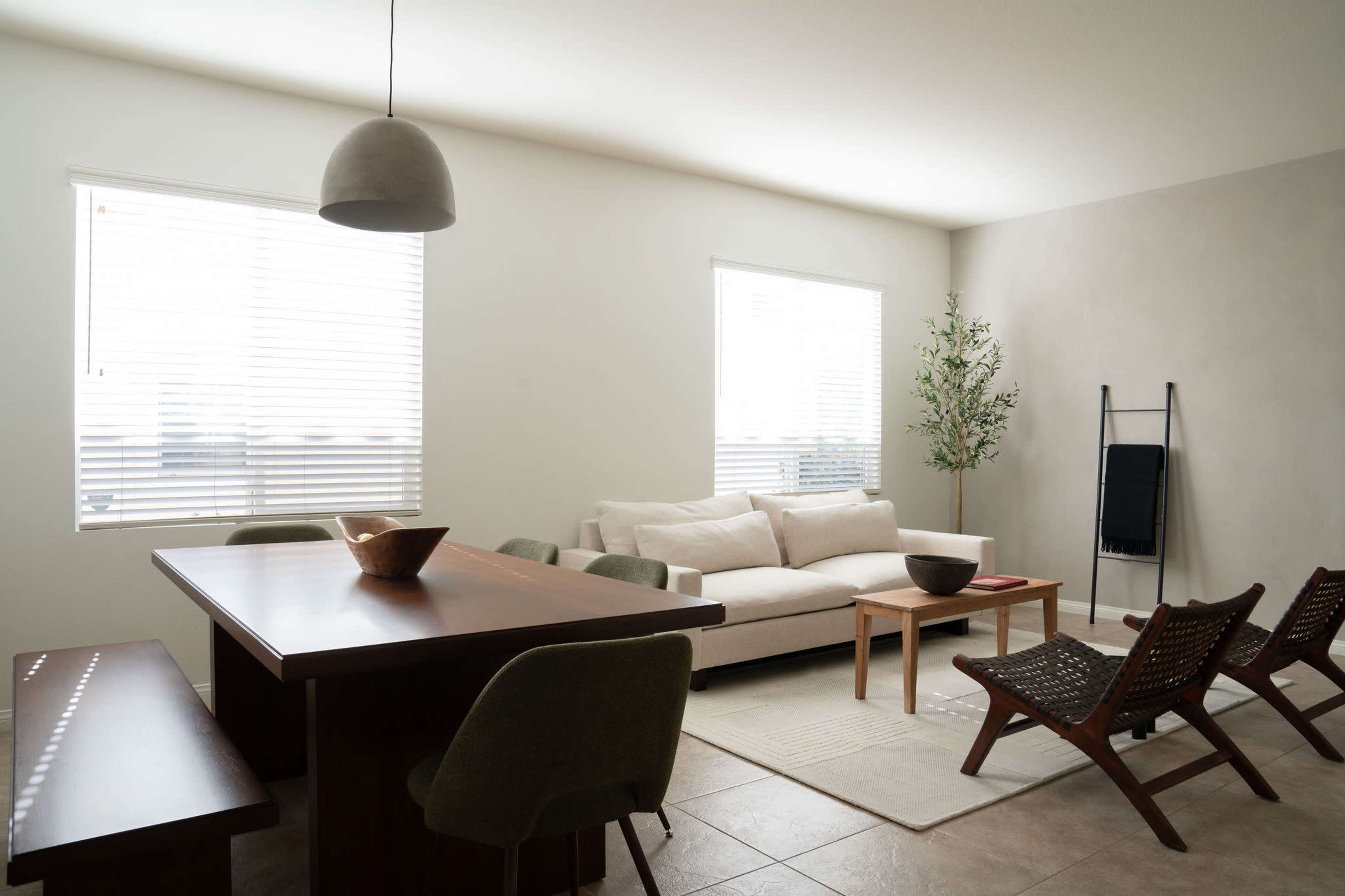 A modern living space features a light-colored sofa, a wooden dining table, and several chairs arranged around a neutral rug.