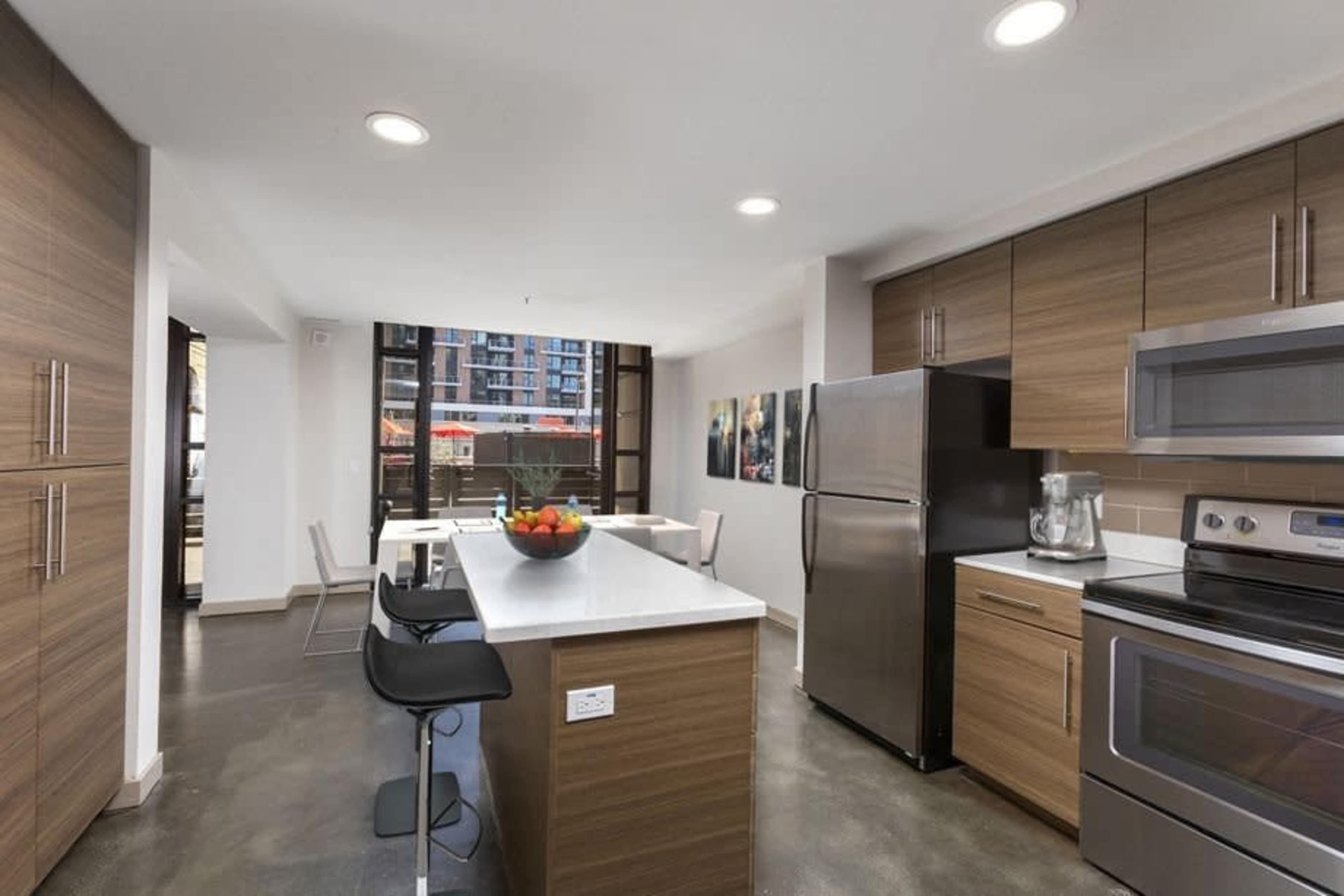 A modern kitchen featuring brown wood cabinetry, stainless steel appliances, and a central island with seating.