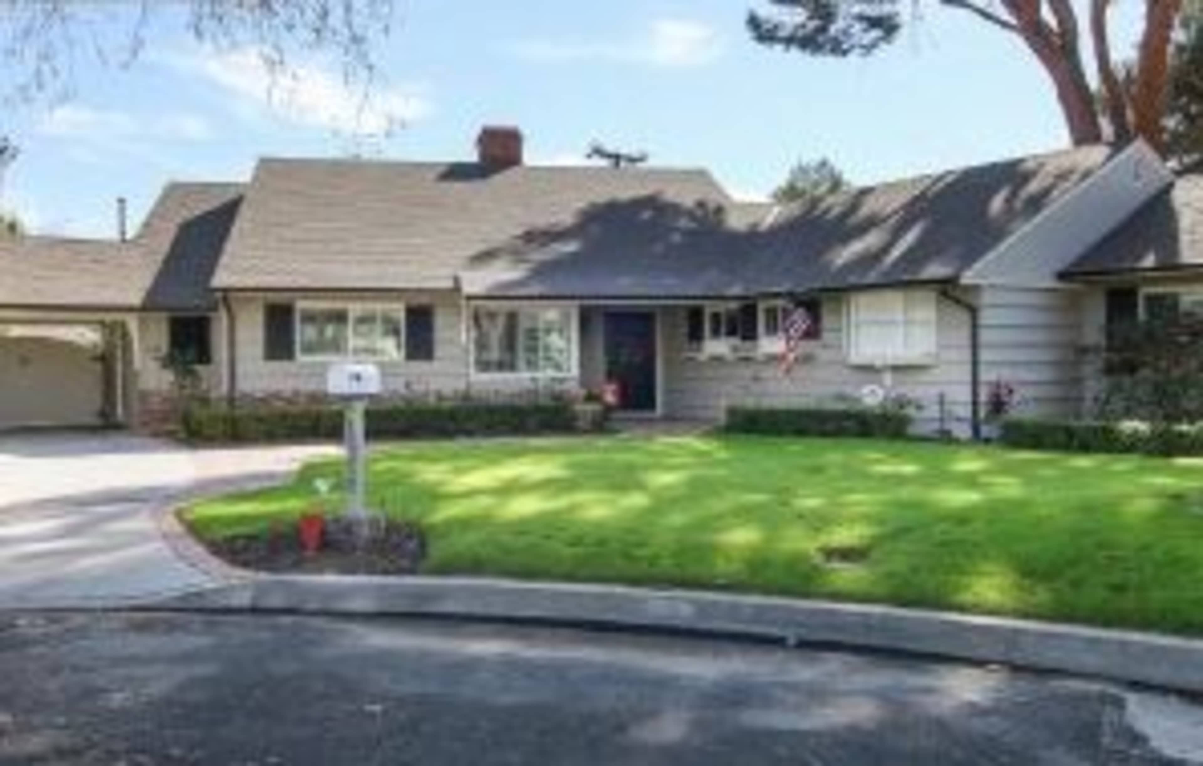 A single-story house with a sloping roof and a front yard, featuring a mailbox and a curved driveway.