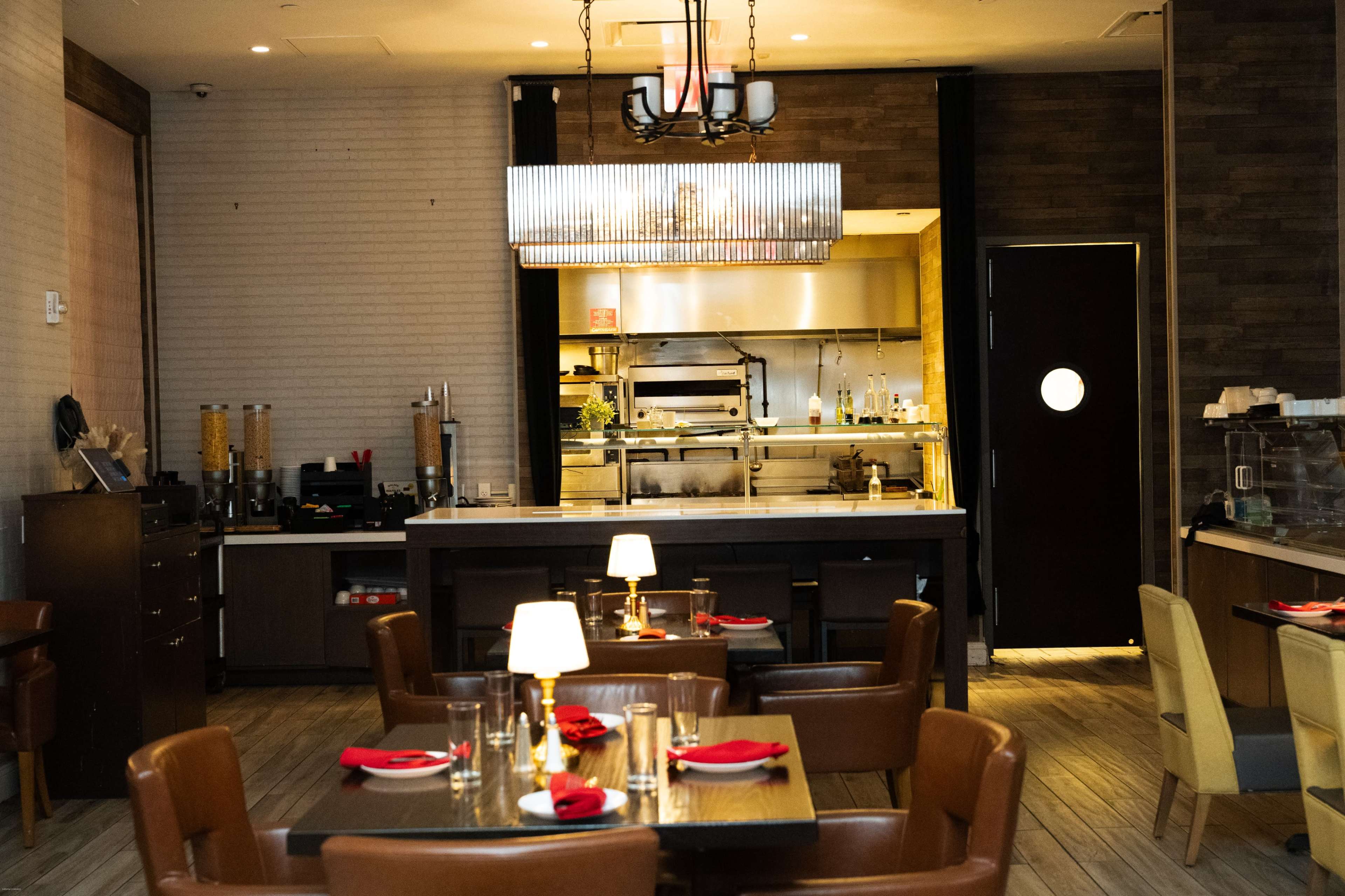 The image shows an upscale restaurant interior with wooden floors, neatly arranged tables, and a visible kitchen area in the background.