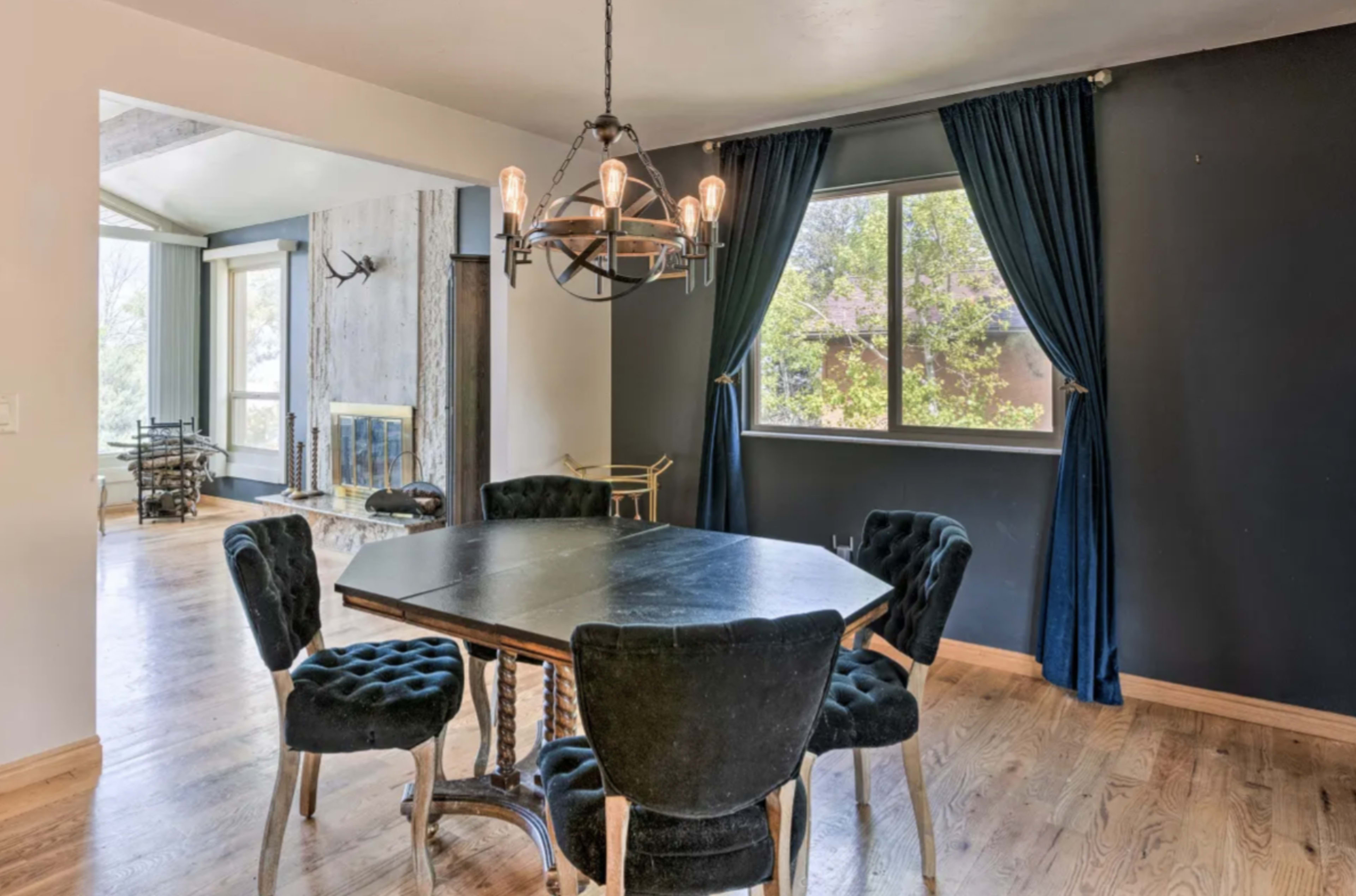 A dining area features a hexagonal table surrounded by six black upholstered chairs with a large window and dark curtains.