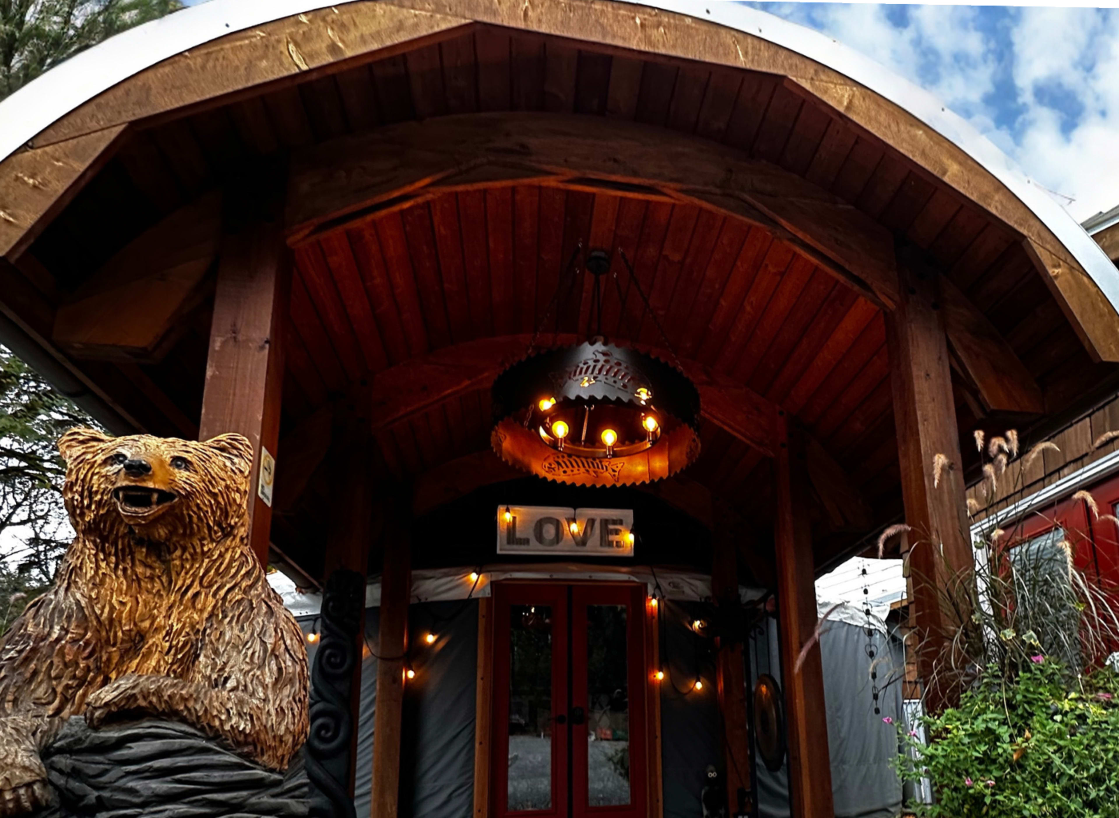 A rustic entrance featuring a wooden archway with a bear sculpture on the left and a chandelier above a sign that reads "LOVE."