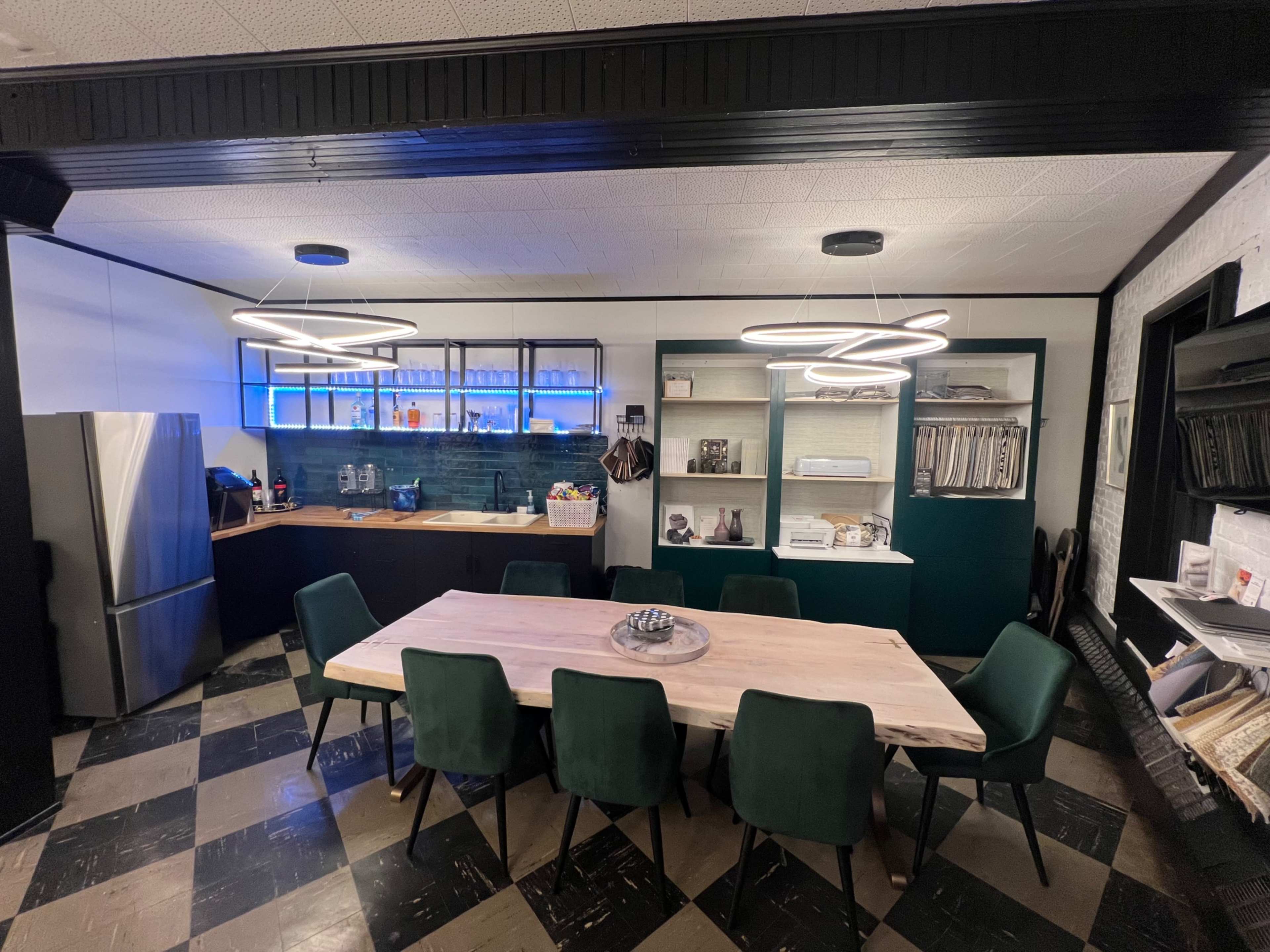 The image shows a modern kitchen and dining area featuring a large wooden table surrounded by green chairs, a stainless steel refrigerator, and blue LED lighting in the cabinetry.