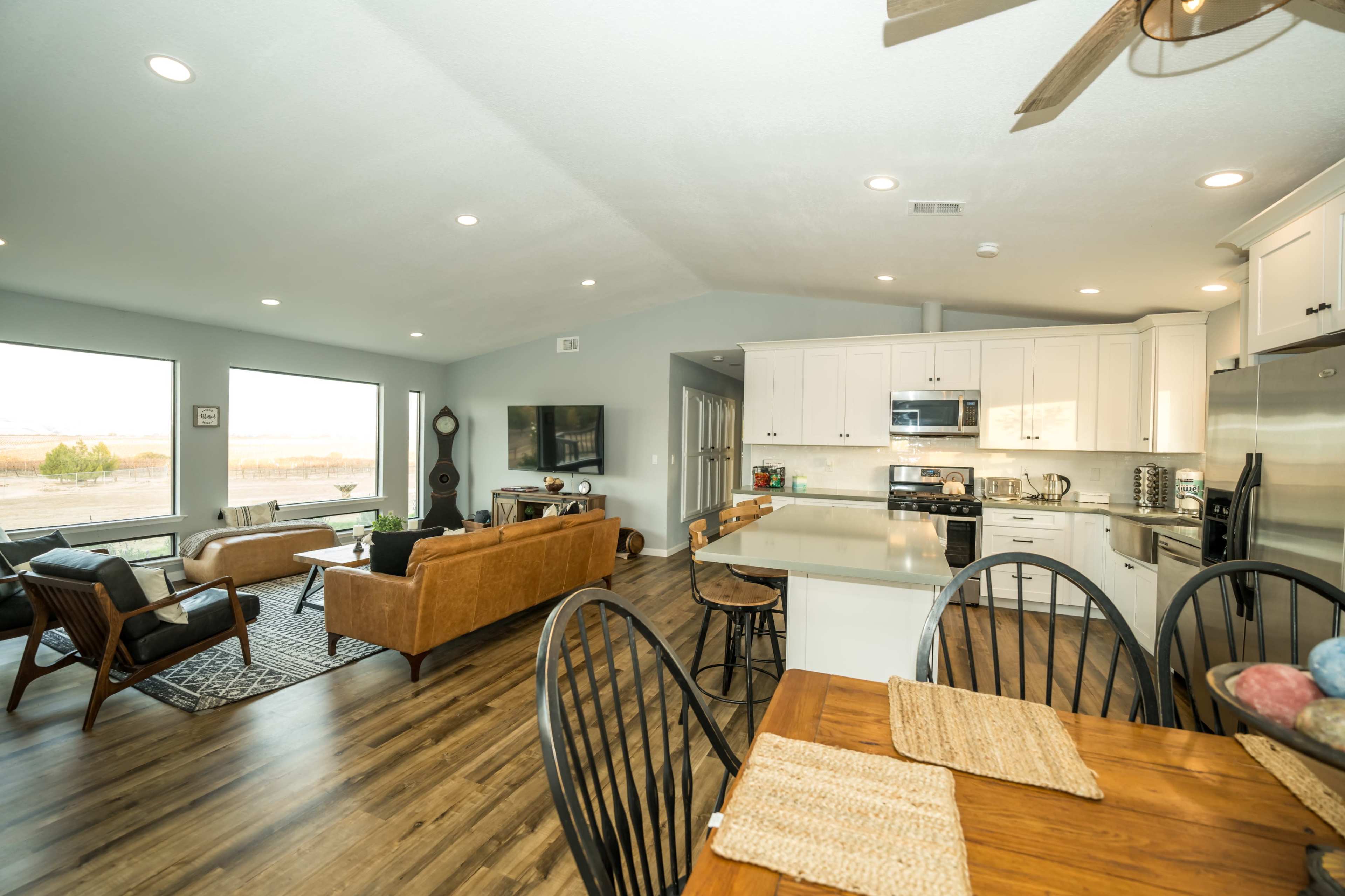 A modern open-concept living and dining area featuring a kitchen with white cabinets, a wooden dining table, and large windows that provide natural light.