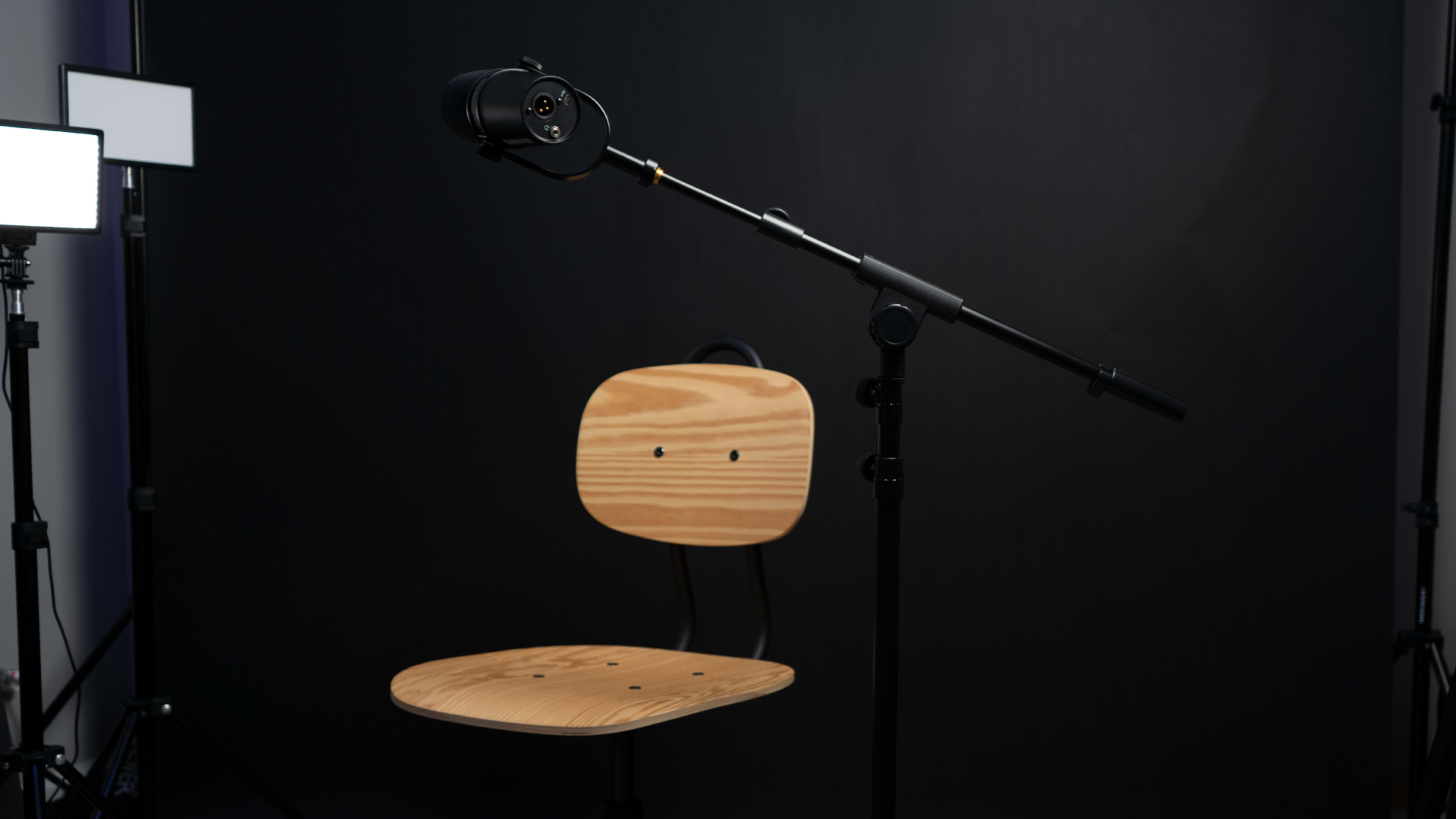 A wooden chair is positioned in front of a black backdrop, with a microphone mounted on a stand nearby.