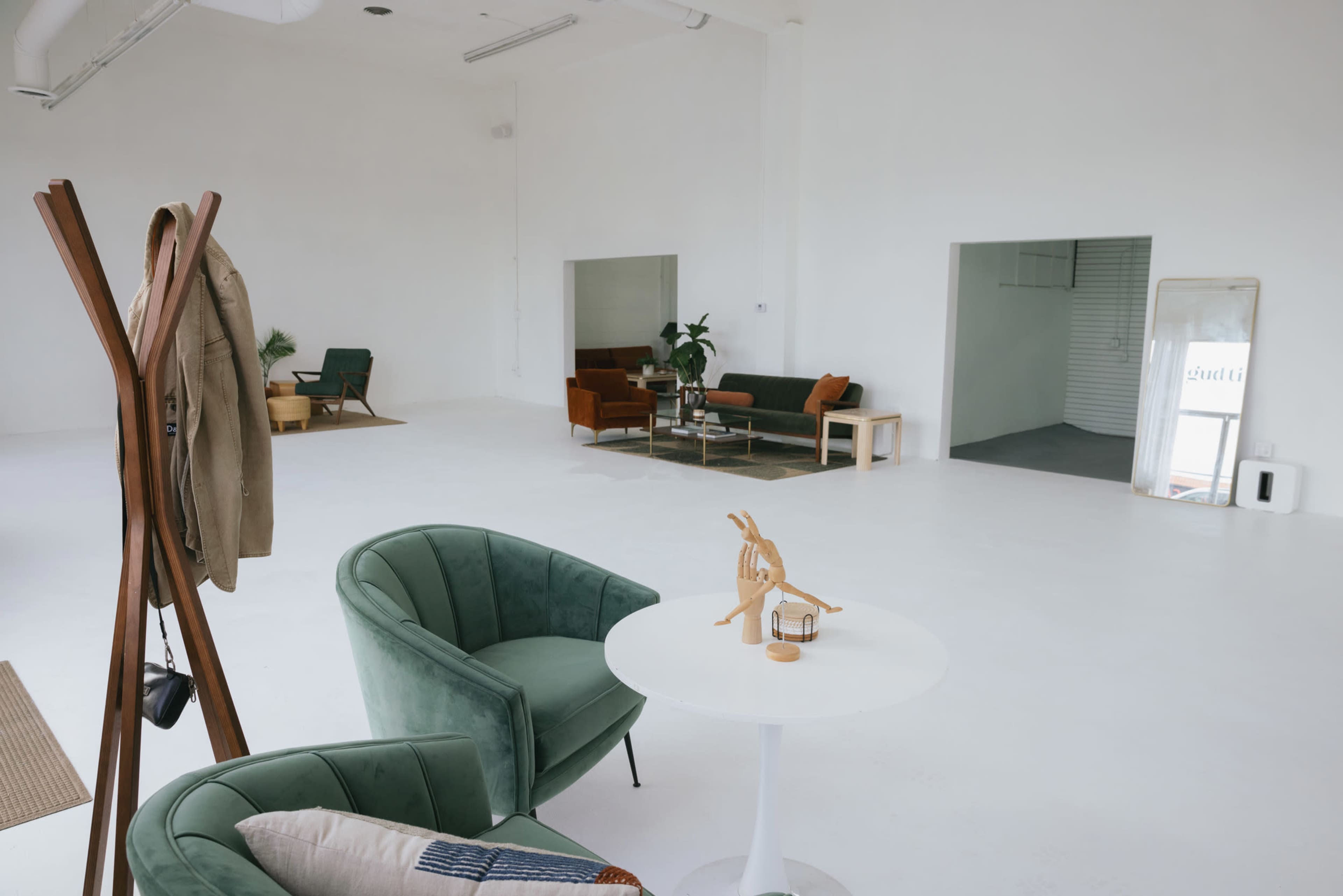 The image shows a spacious, minimalist interior with modern furniture, including green chairs, a small table, and a few couches in a light-filled room.