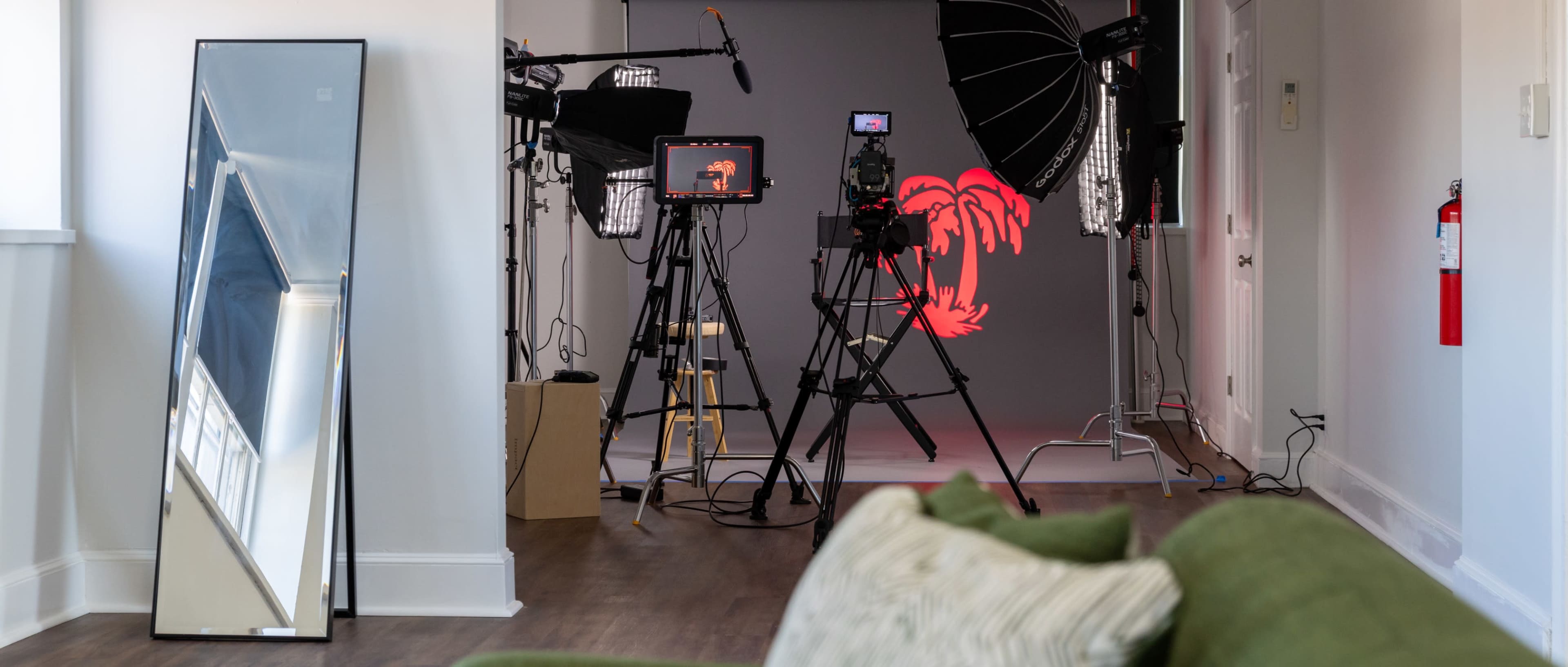 The image shows a photography studio setup with lighting equipment, cameras, and a reflective mirror positioned in a hallway.