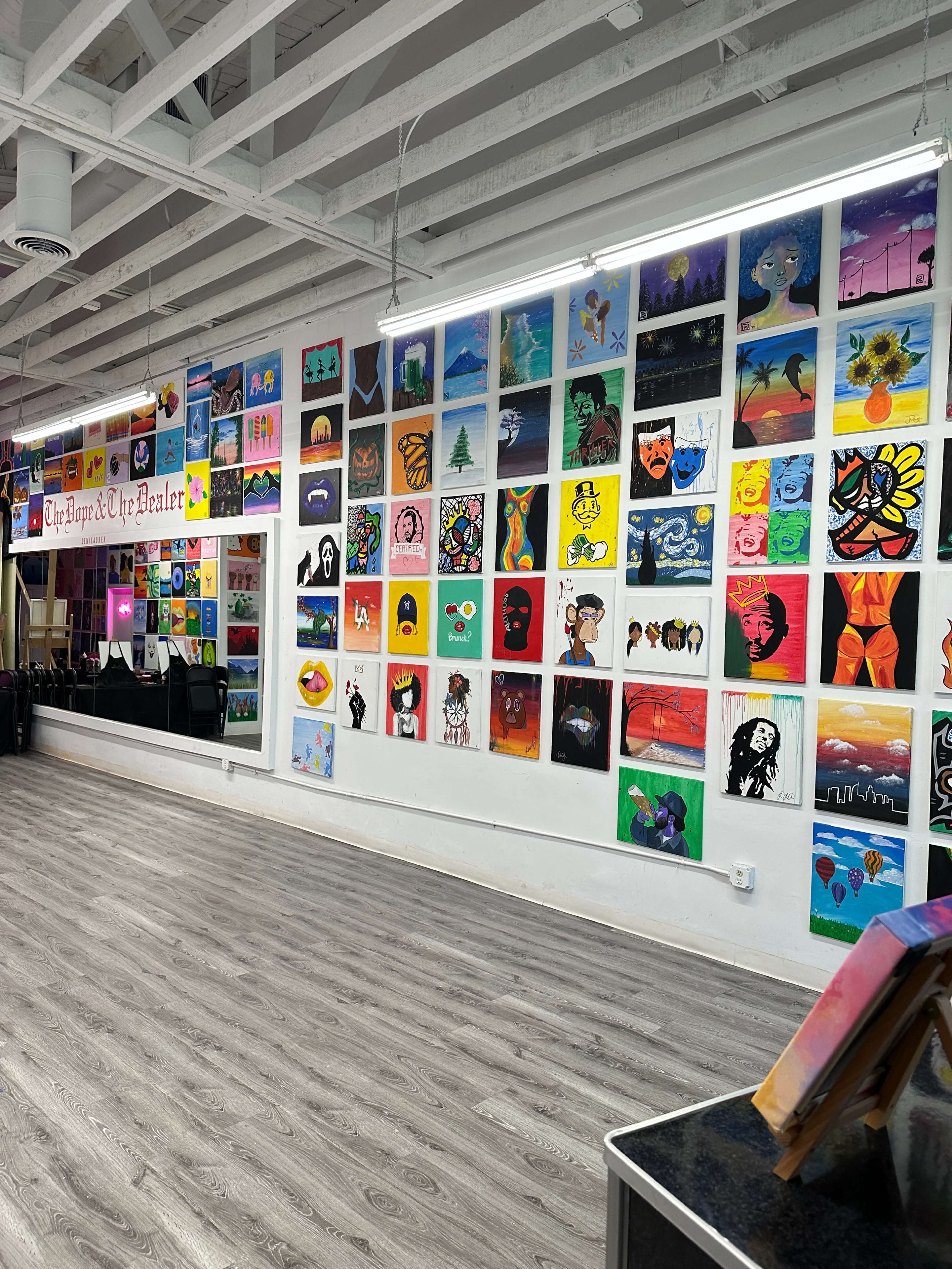 The image shows a brightly lit room with a wall covered in colorful artwork, featuring various paintings and illustrations hung from floor to ceiling.