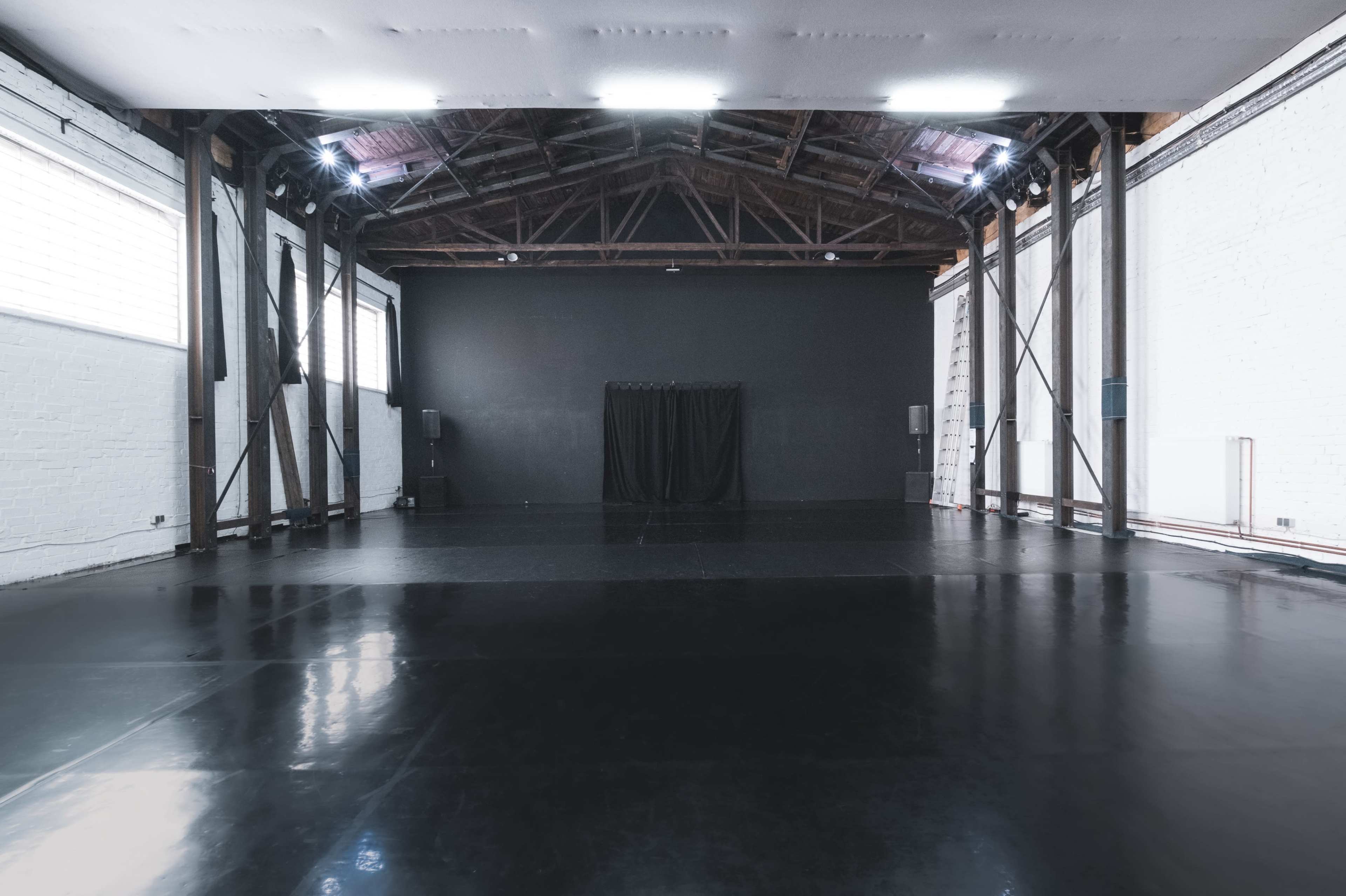 A large, empty studio space with polished black flooring and high wooden beams.