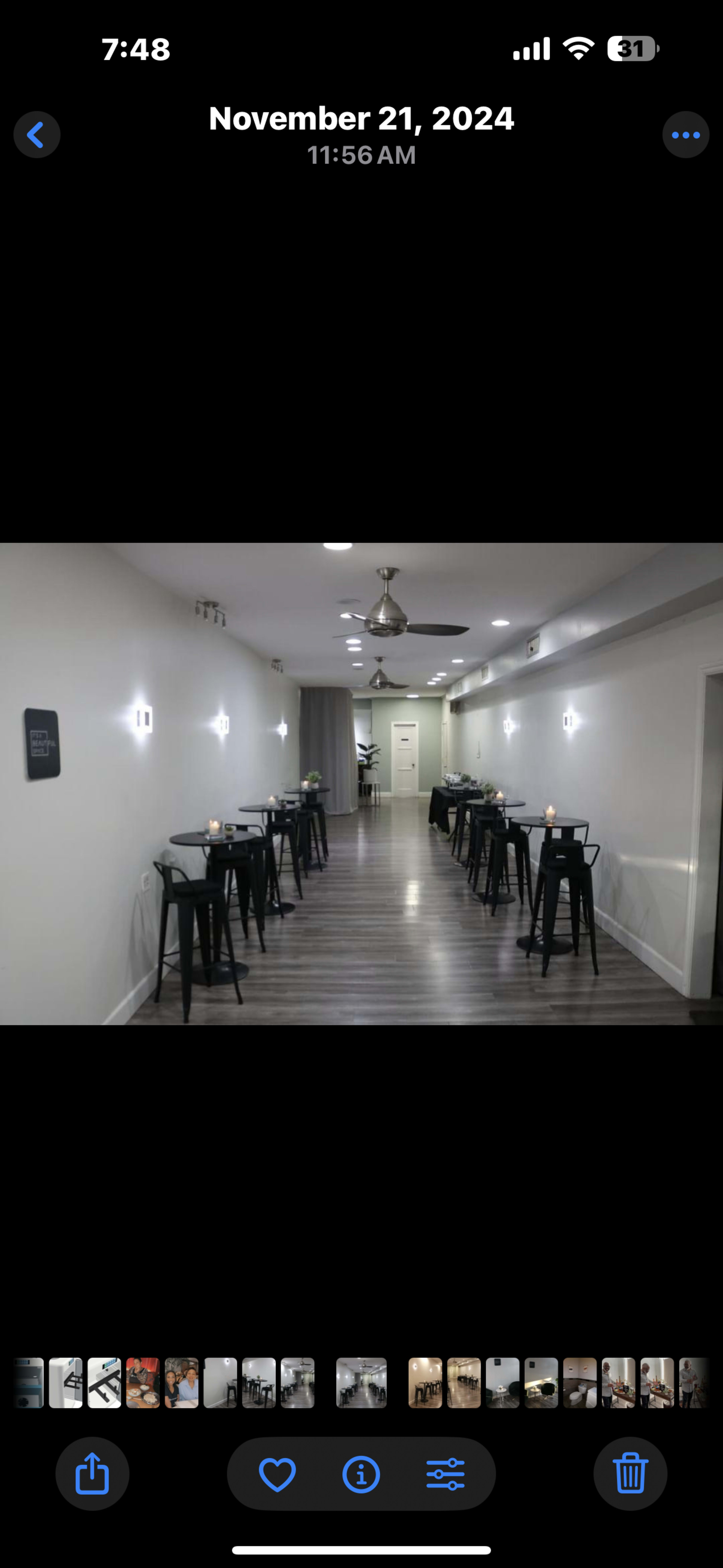 The image shows a well-lit, narrow corridor with minimalist decor, featuring several tables along the sides and soft lighting.