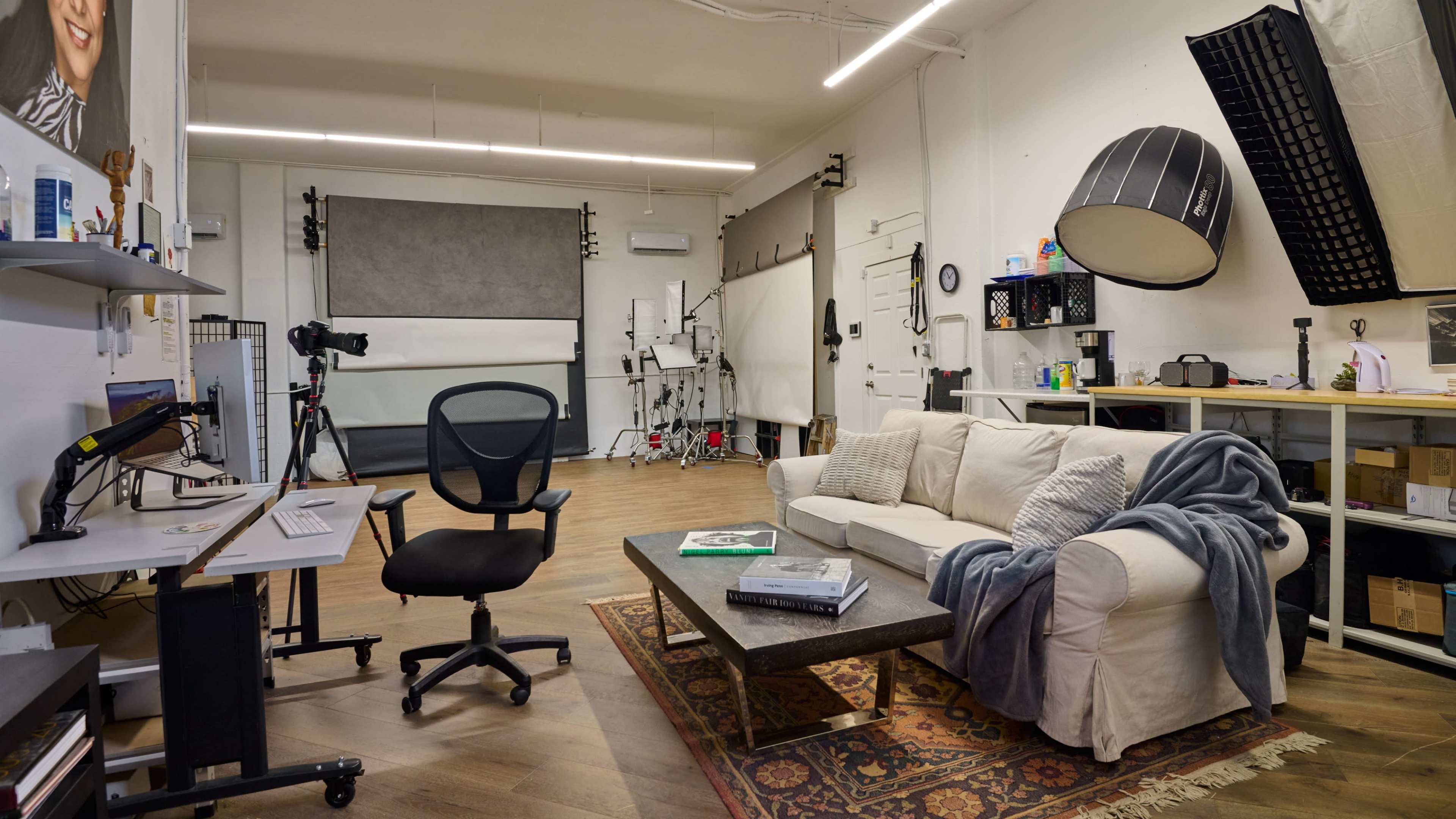 A well-organized photography studio featuring a sofa, a coffee table, a desk with a computer, and various photography equipment.
