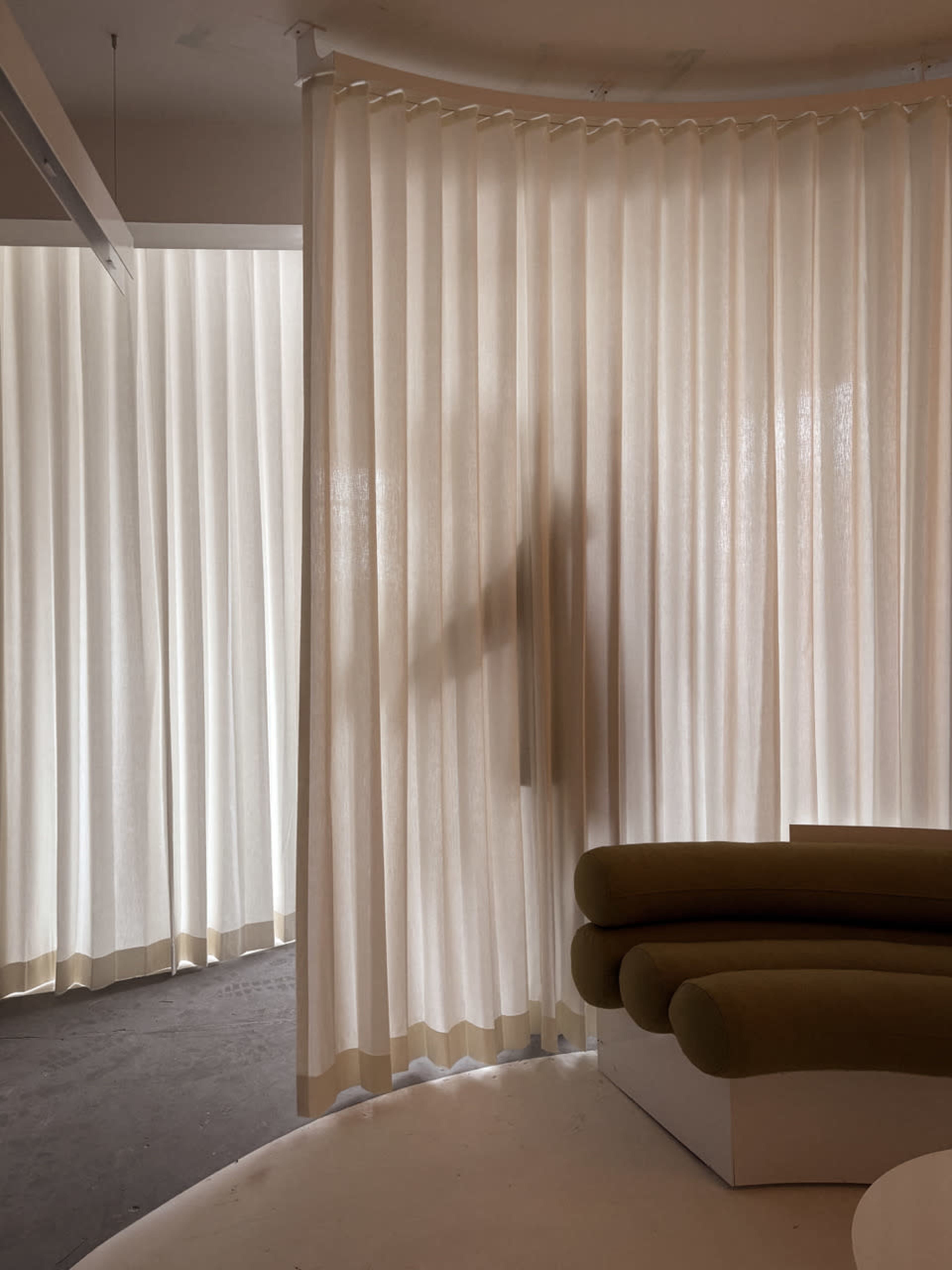 A softly-lit interior features sheer curtains that create a separation between spaces, with a shadowy figure visible behind them.