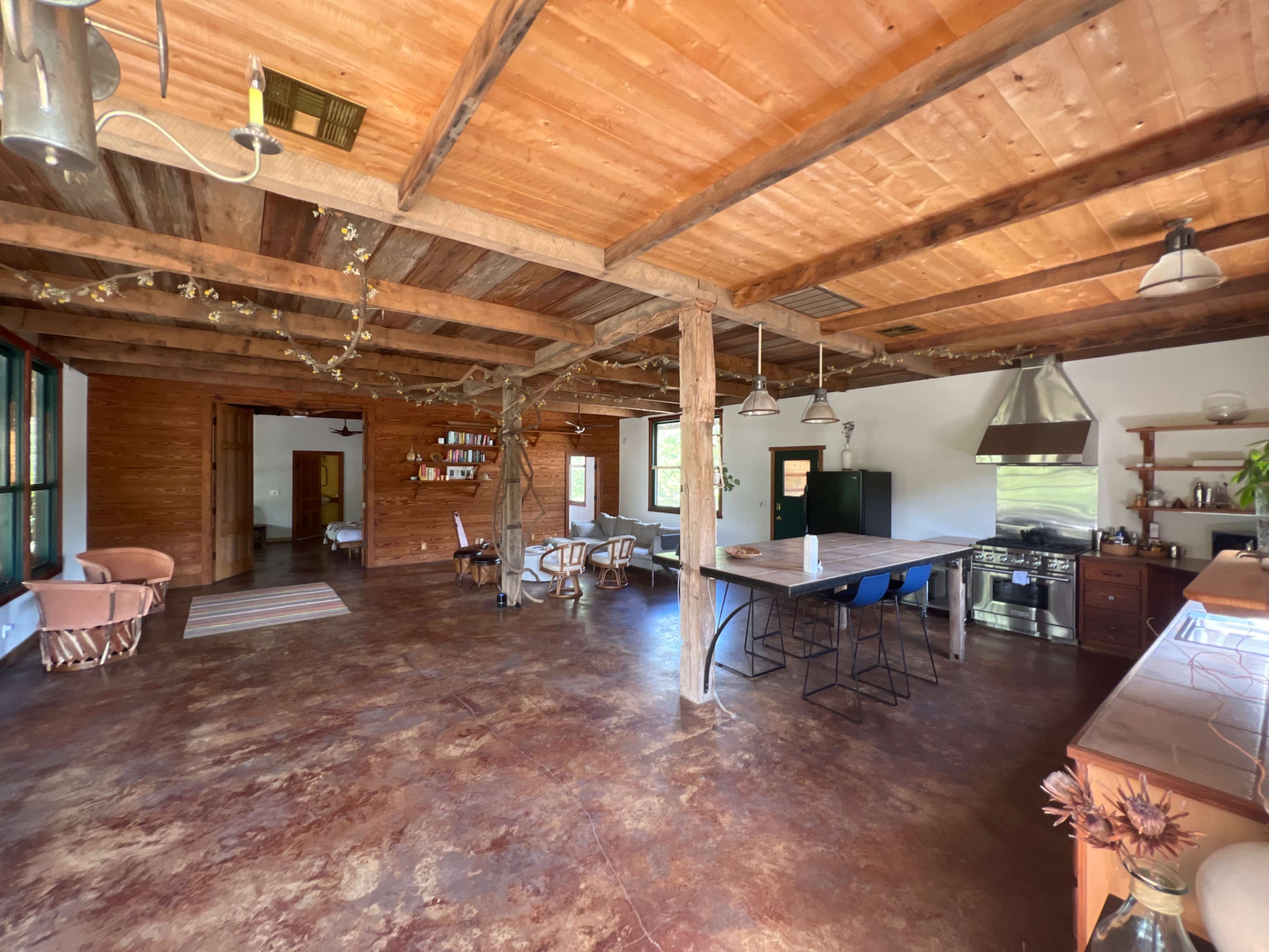 An open-concept interior of a rustic living space featuring wooden ceilings, a kitchen area with modern appliances, and seating arrangements.