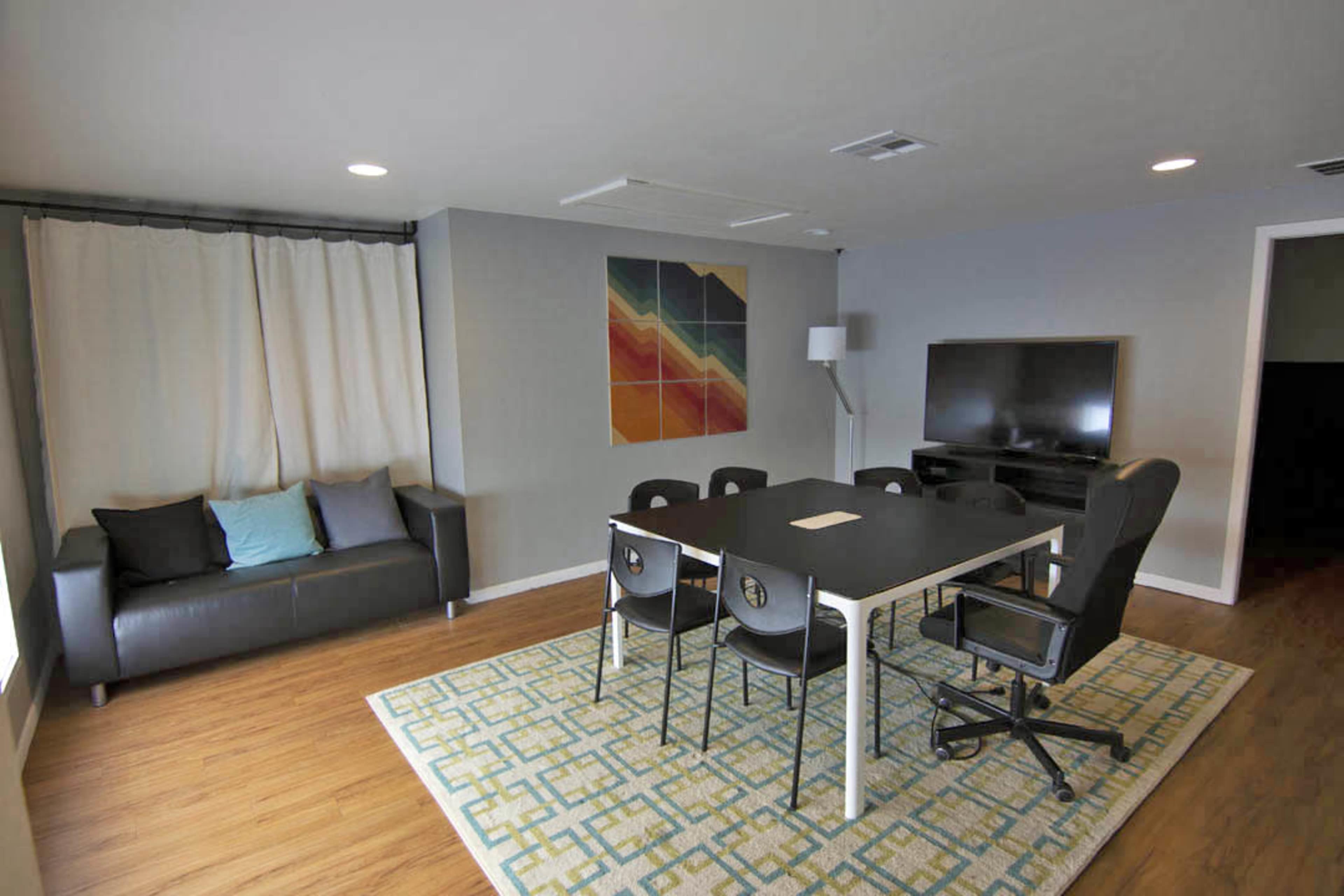 A modern meeting room with a black table, four chairs, a couch, a television, and a colorful wall art piece.