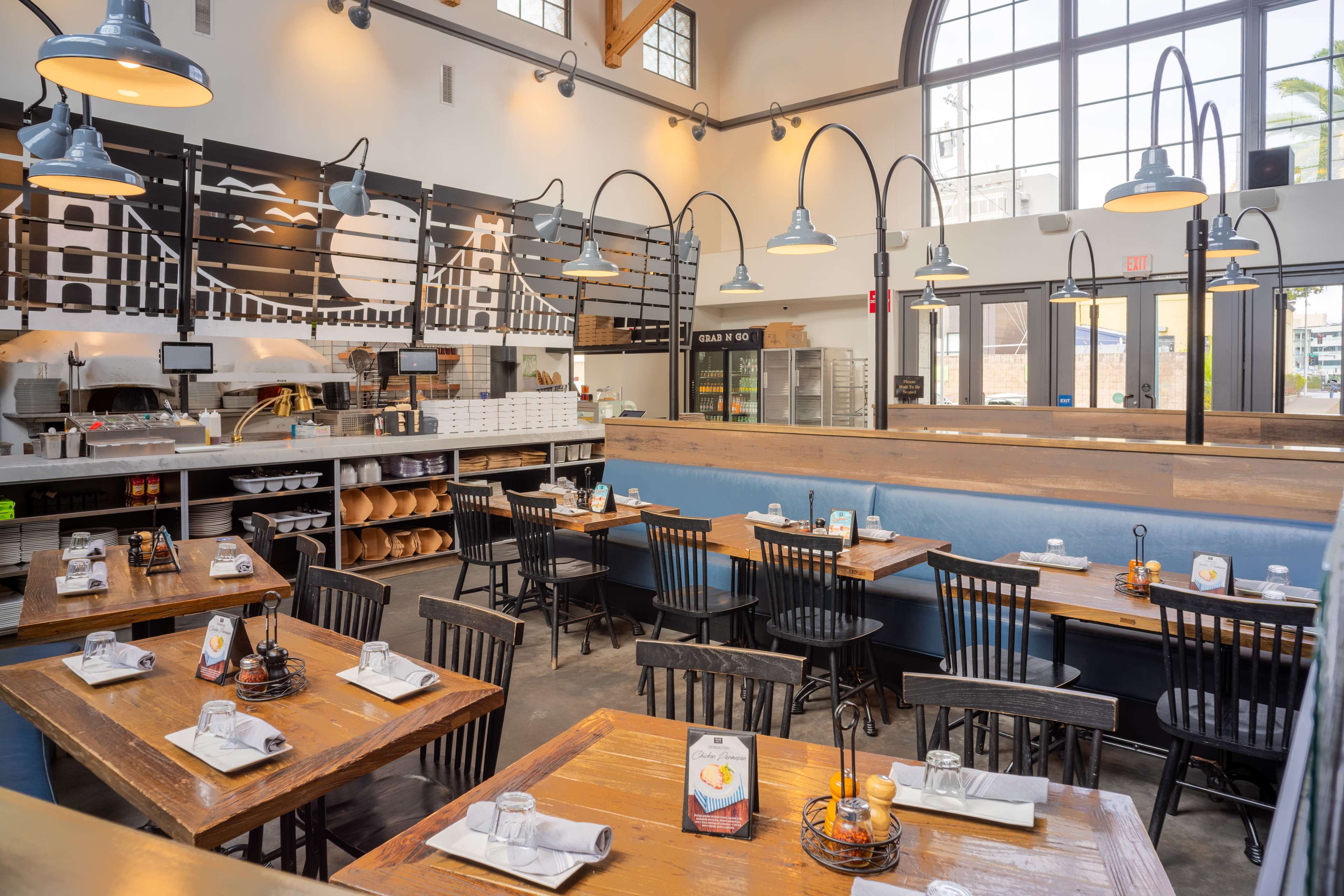 The image shows a modern restaurant interior with wooden tables and black chairs, large windows, and a stylish overhead light fixture.