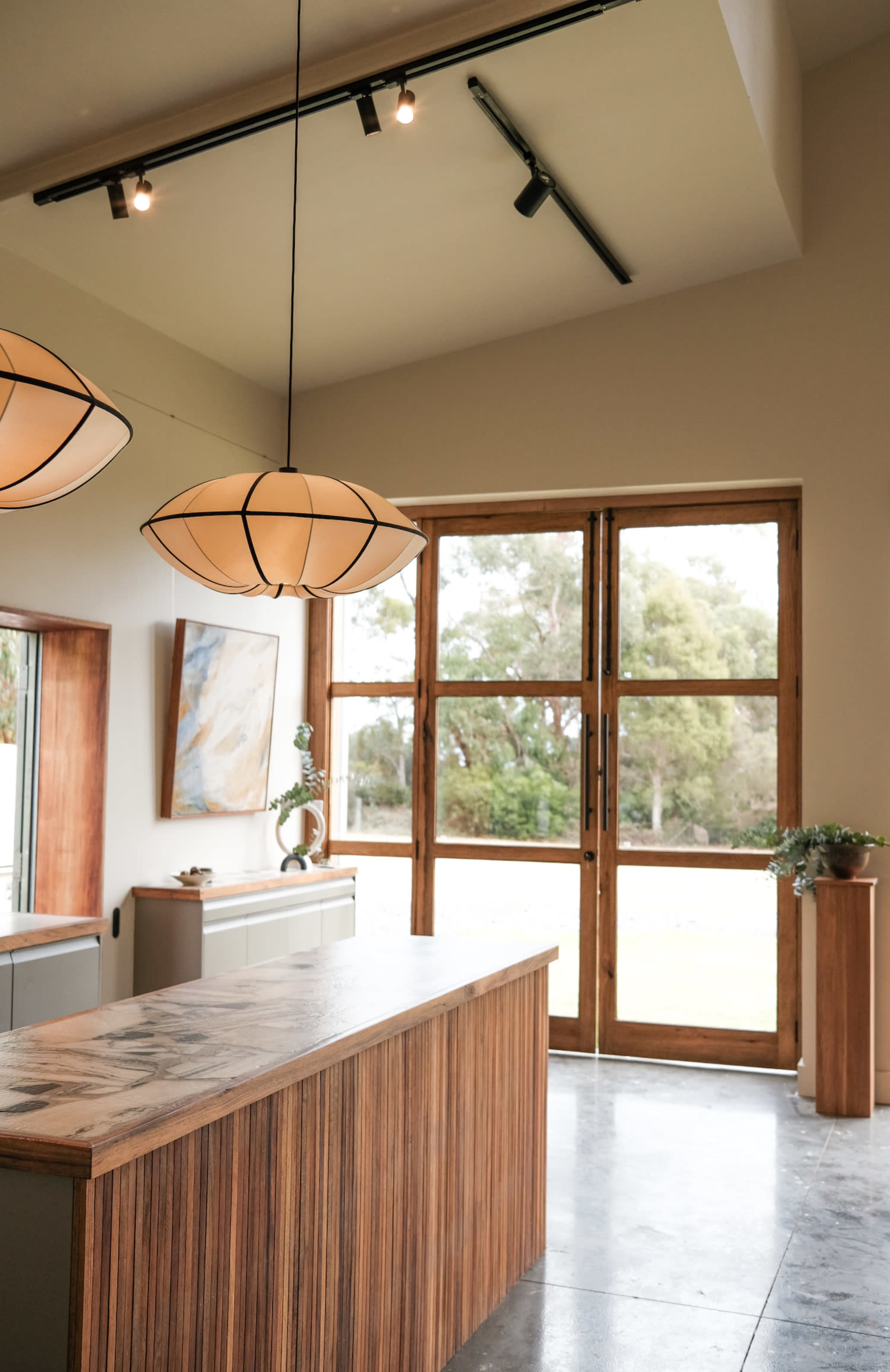 A modern reception area with a wooden front desk, two pendant lights, and large glass doors leading to an outdoor view.
