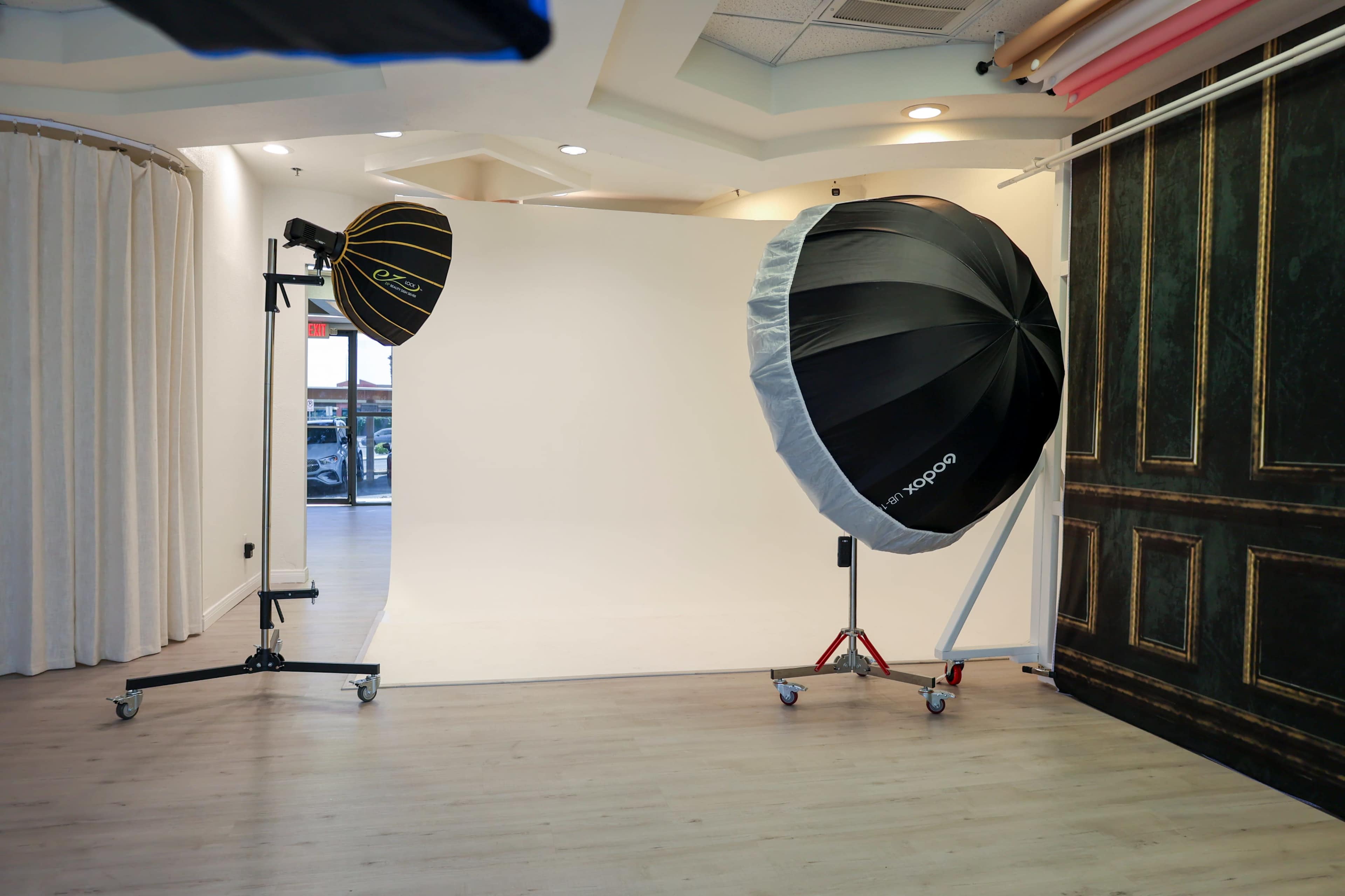 The image shows a photography studio with a blank white backdrop and two large light modifiers positioned on either side.