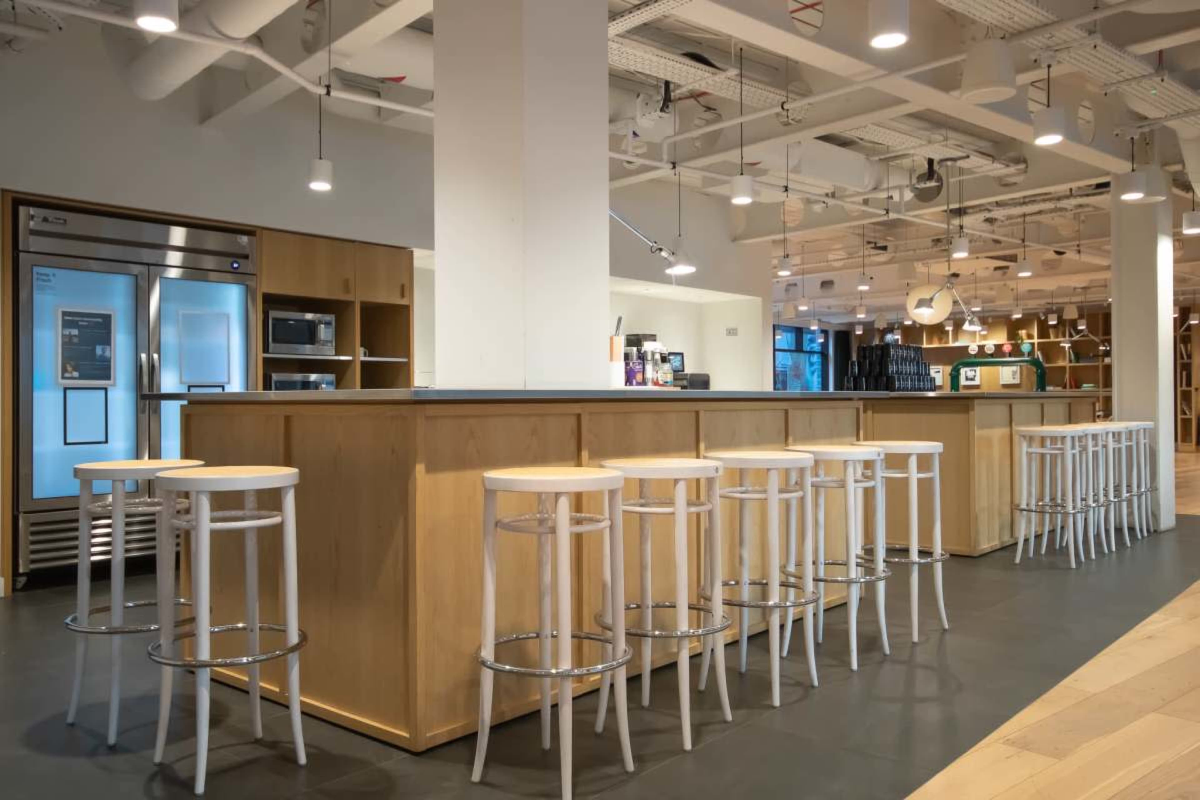 The image shows a modern café interior with a wooden counter and several white bar stools arranged in front.