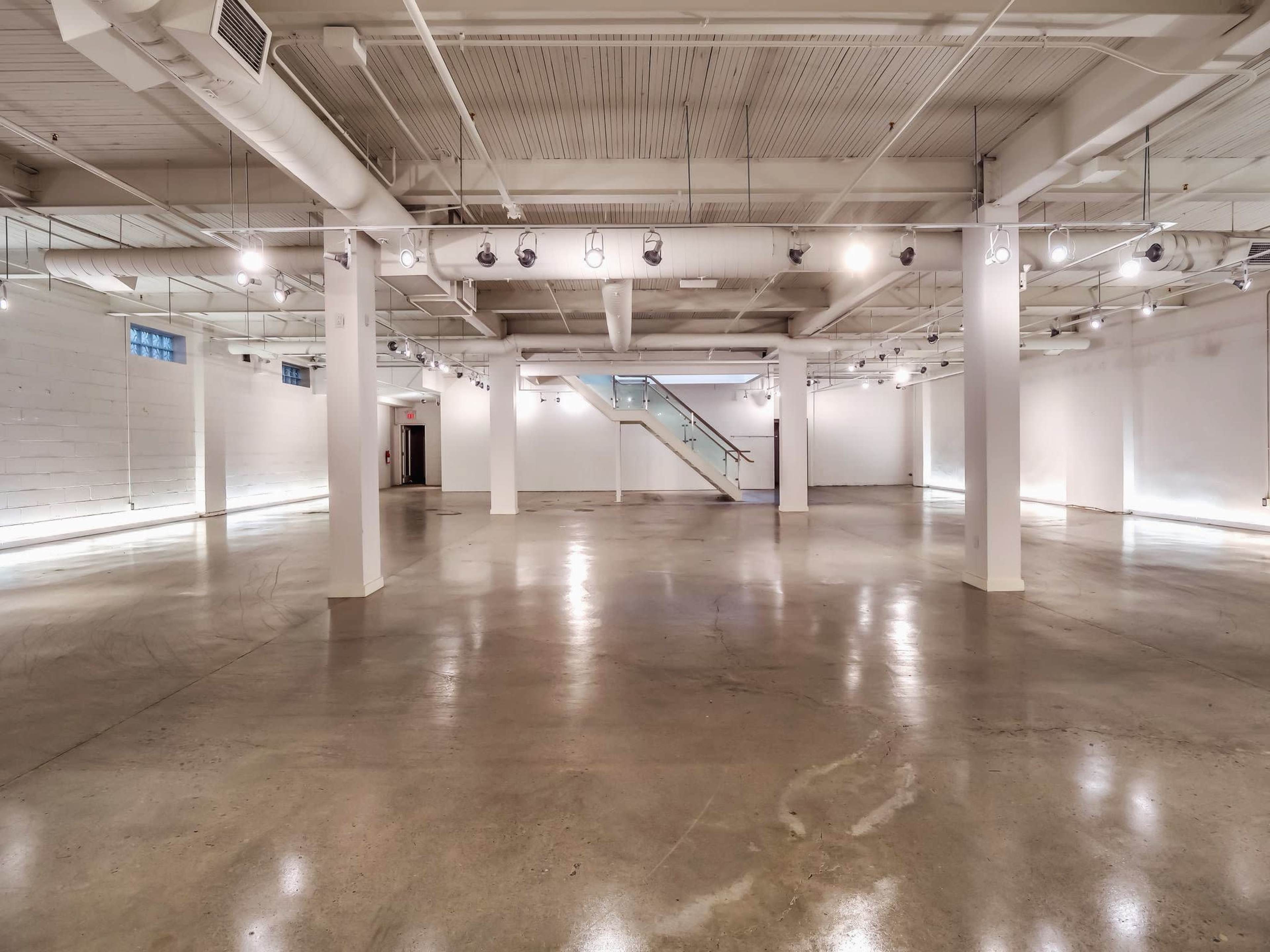 A spacious, empty interior of a commercial building with concrete floors and bright overhead lighting.