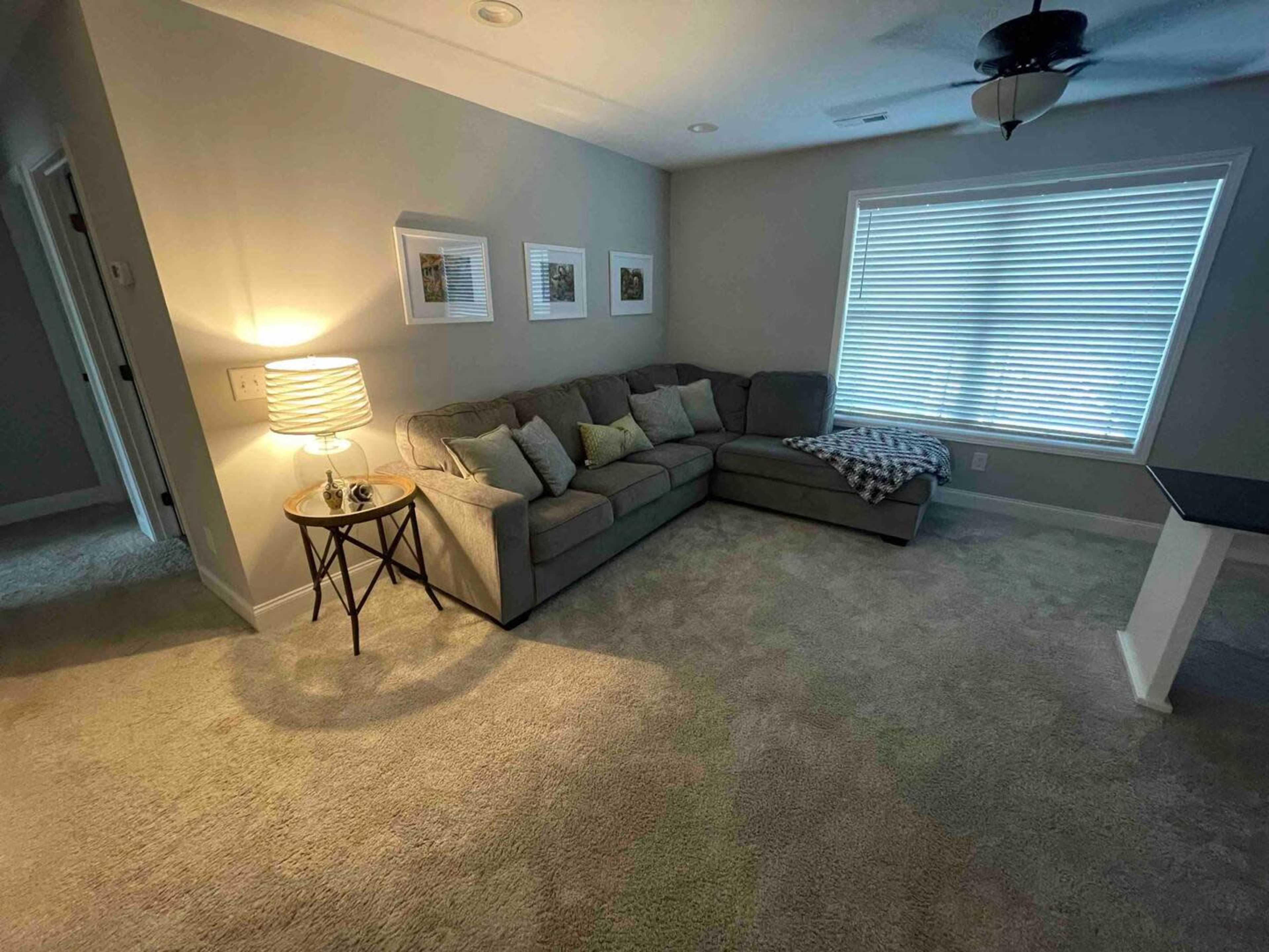 A living room features a sectional couch, a side table with a lamp, and a window with blinds.
