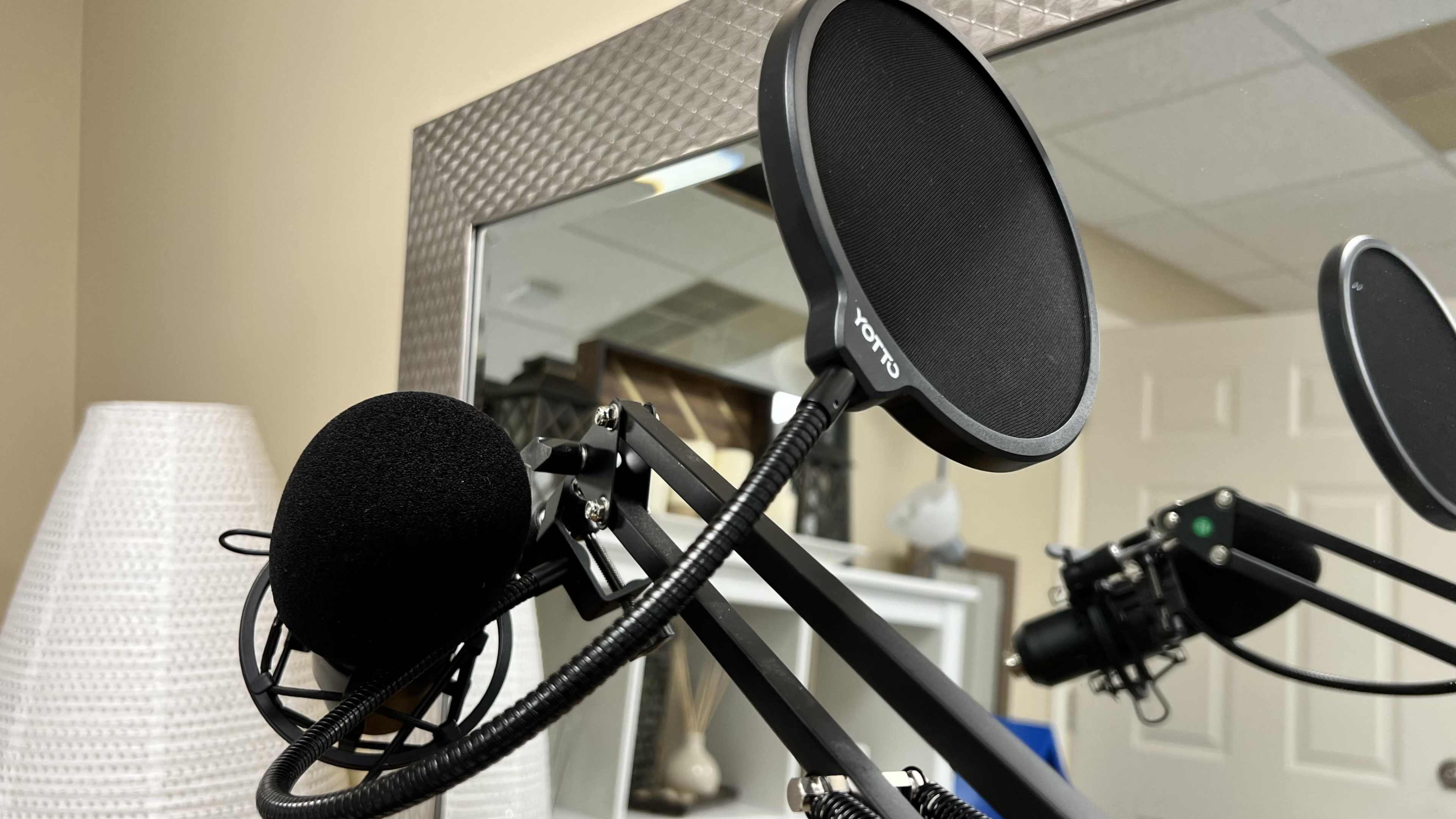 A black microphone with a pop filter is positioned near a mirror in an office setting.