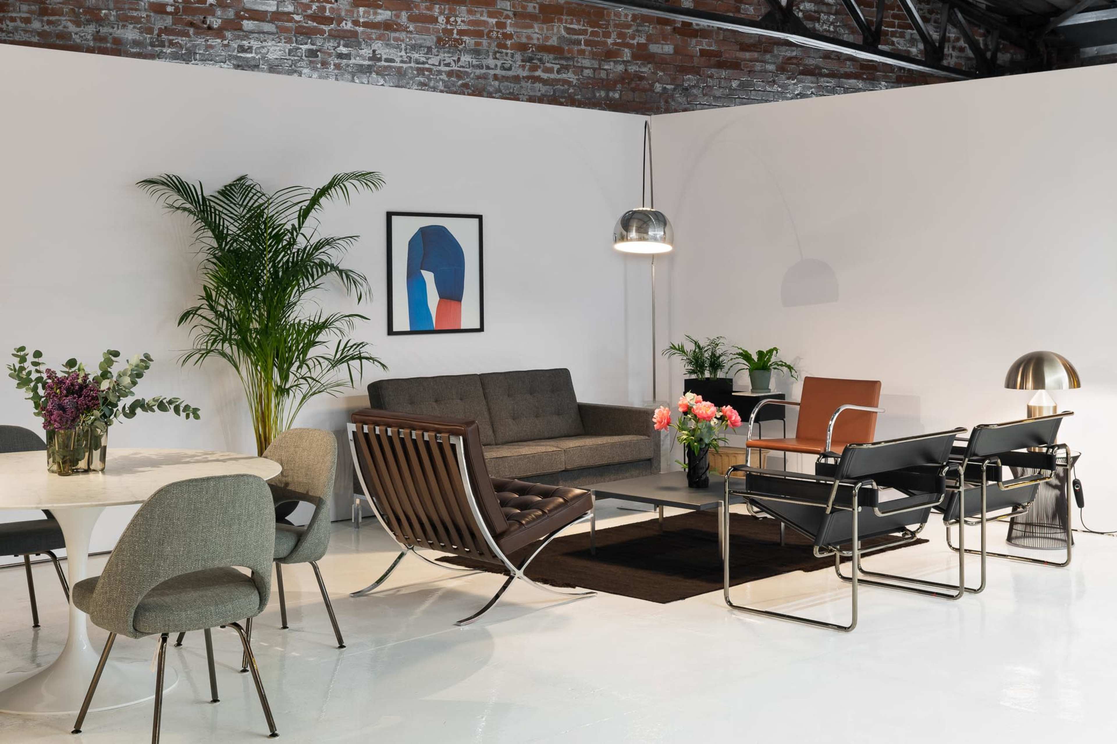 The image shows a modern interior living space featuring a sofa, chairs, a dining table, and decorative plants against a brick wall.