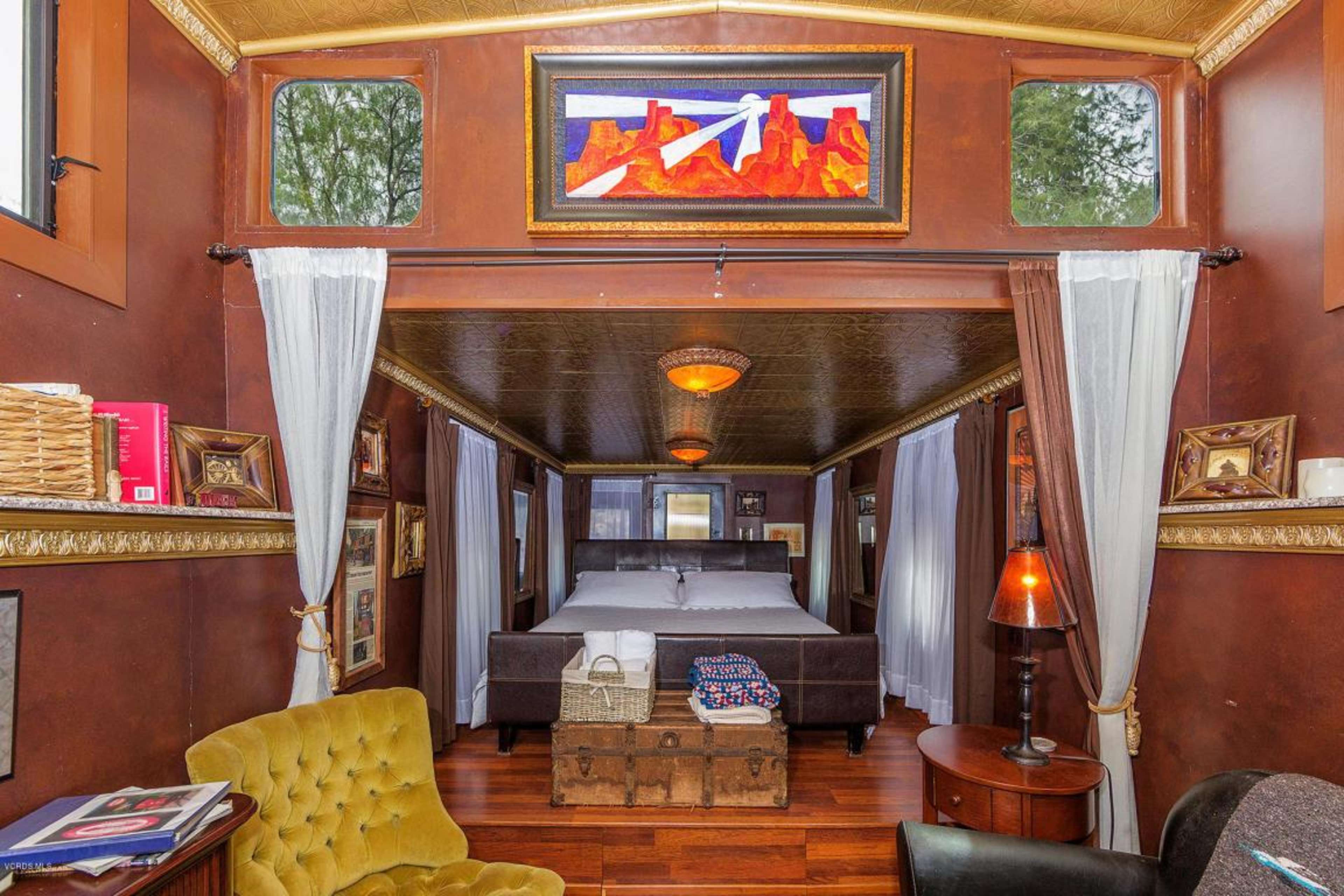 A cozy interior of a bedroom featuring a bed, brown walls adorned with framed artworks, and a sitting area with a yellow armchair.