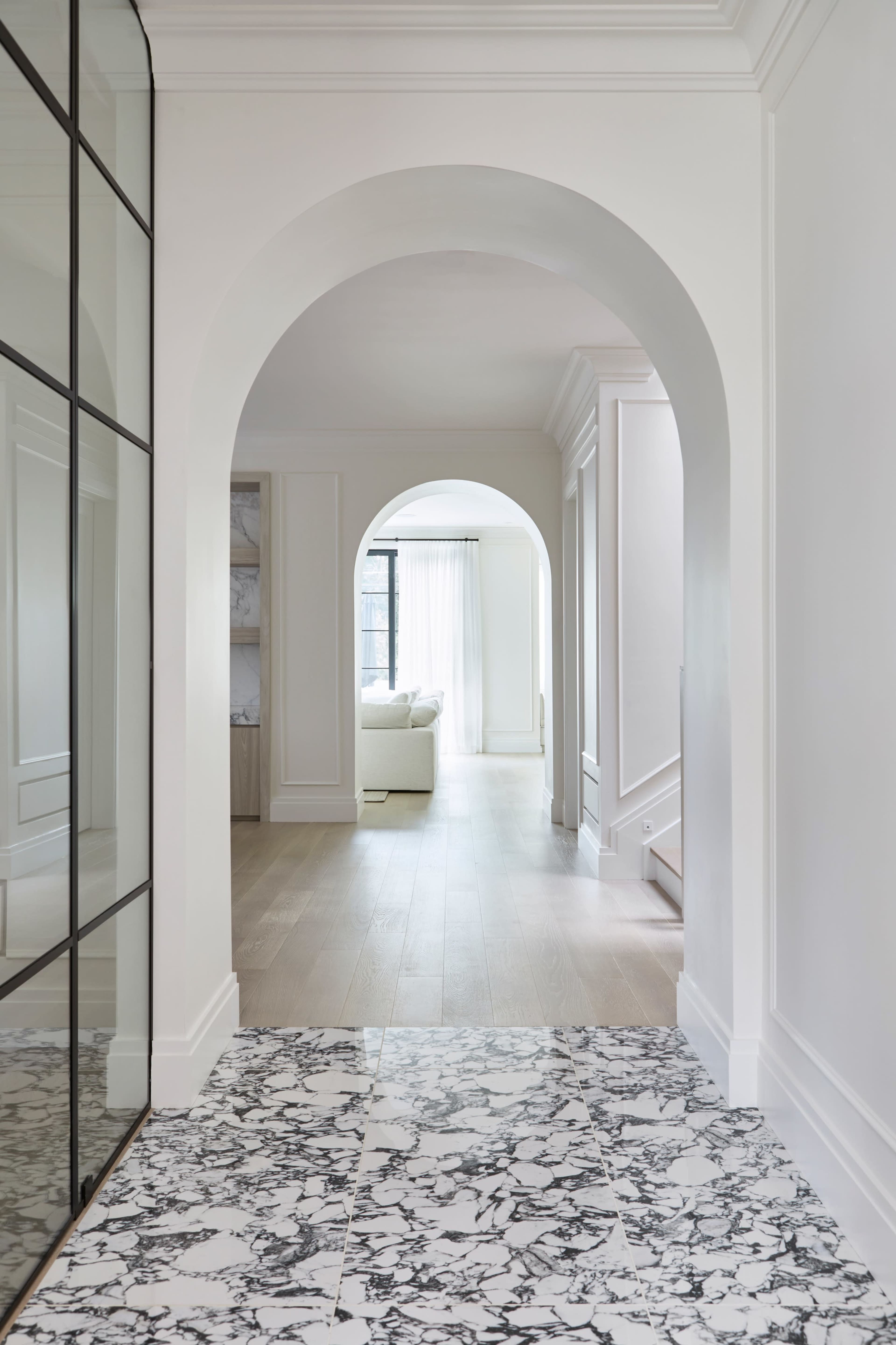 A hallway features a marble floor and large, arched openings leading to a well-lit living area.