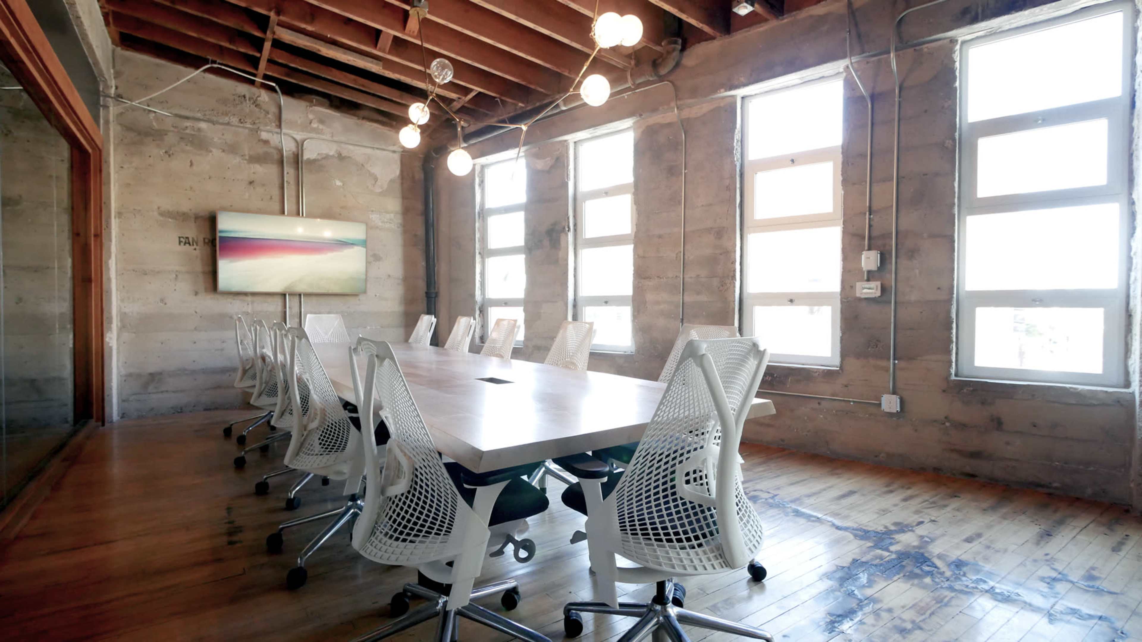 A conference room features a long table surrounded by modern chairs, with large windows and industrial-style lighting.