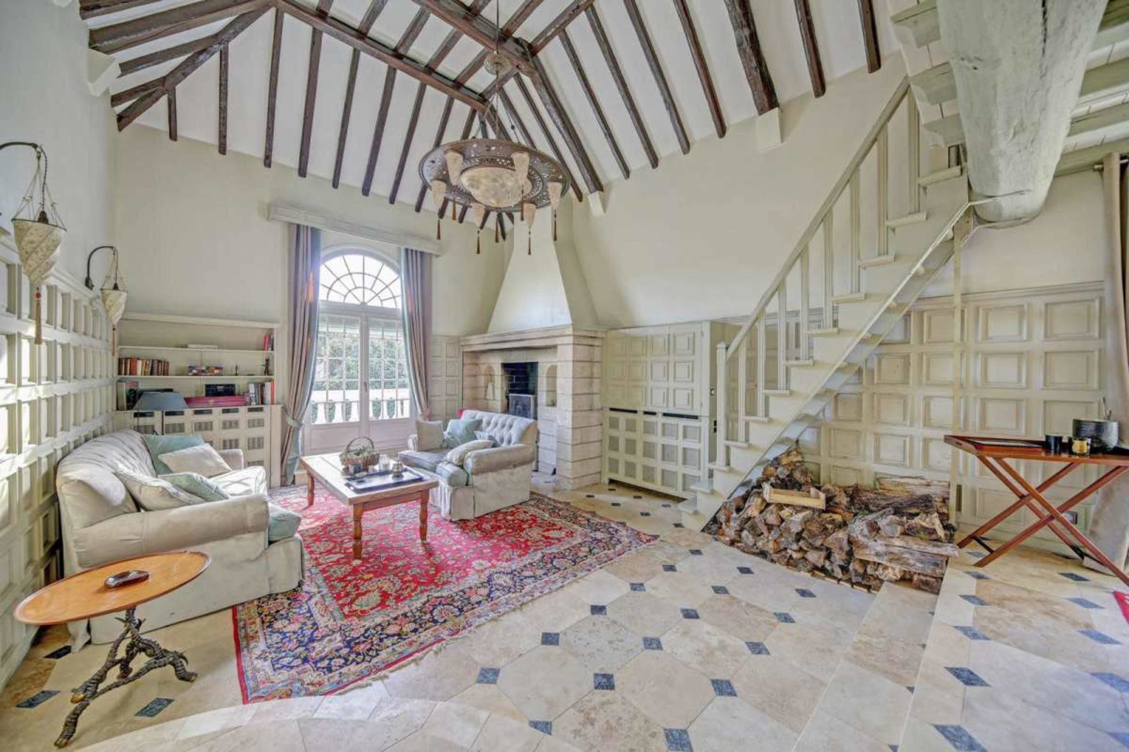 The image depicts a cozy living room with high, beamed ceilings, a fireplace, and a staircase leading to an upper level.