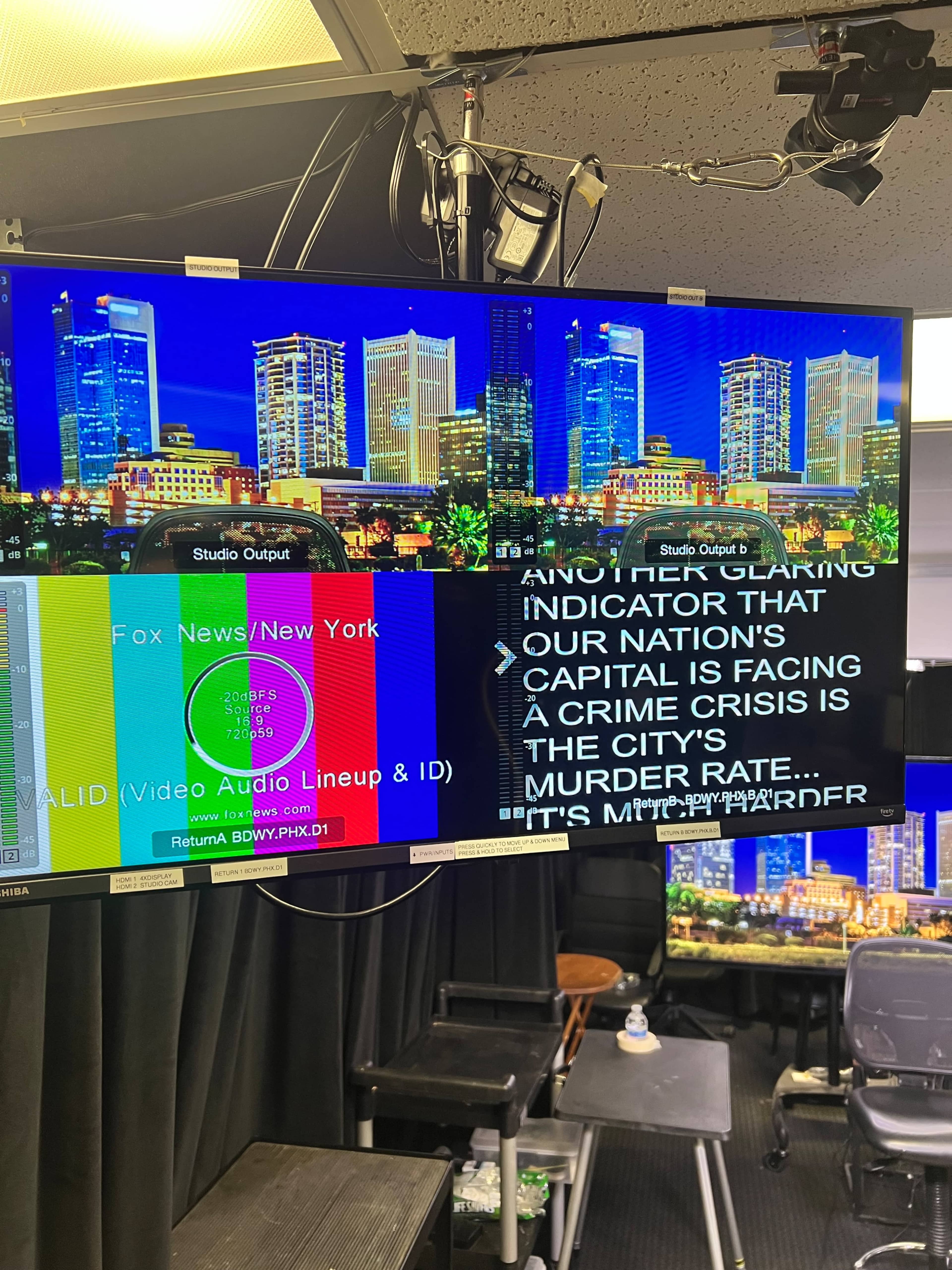 The image shows a television studio setup with two screens displaying city skyline graphics and on-screen text about a crime crisis.