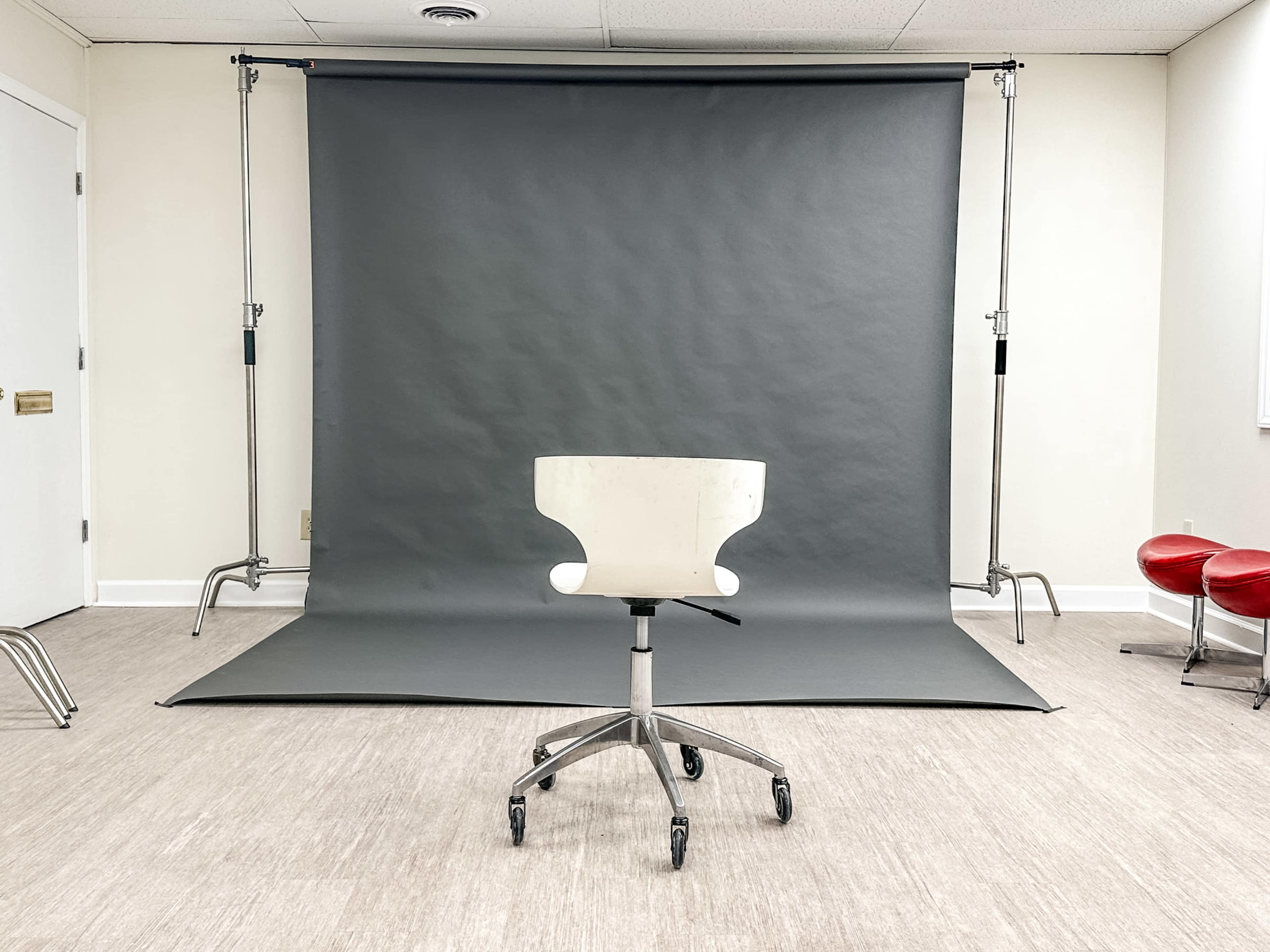 A white office chair on wheels sits in front of a gray backdrop set up on a clean, light-colored floor.
