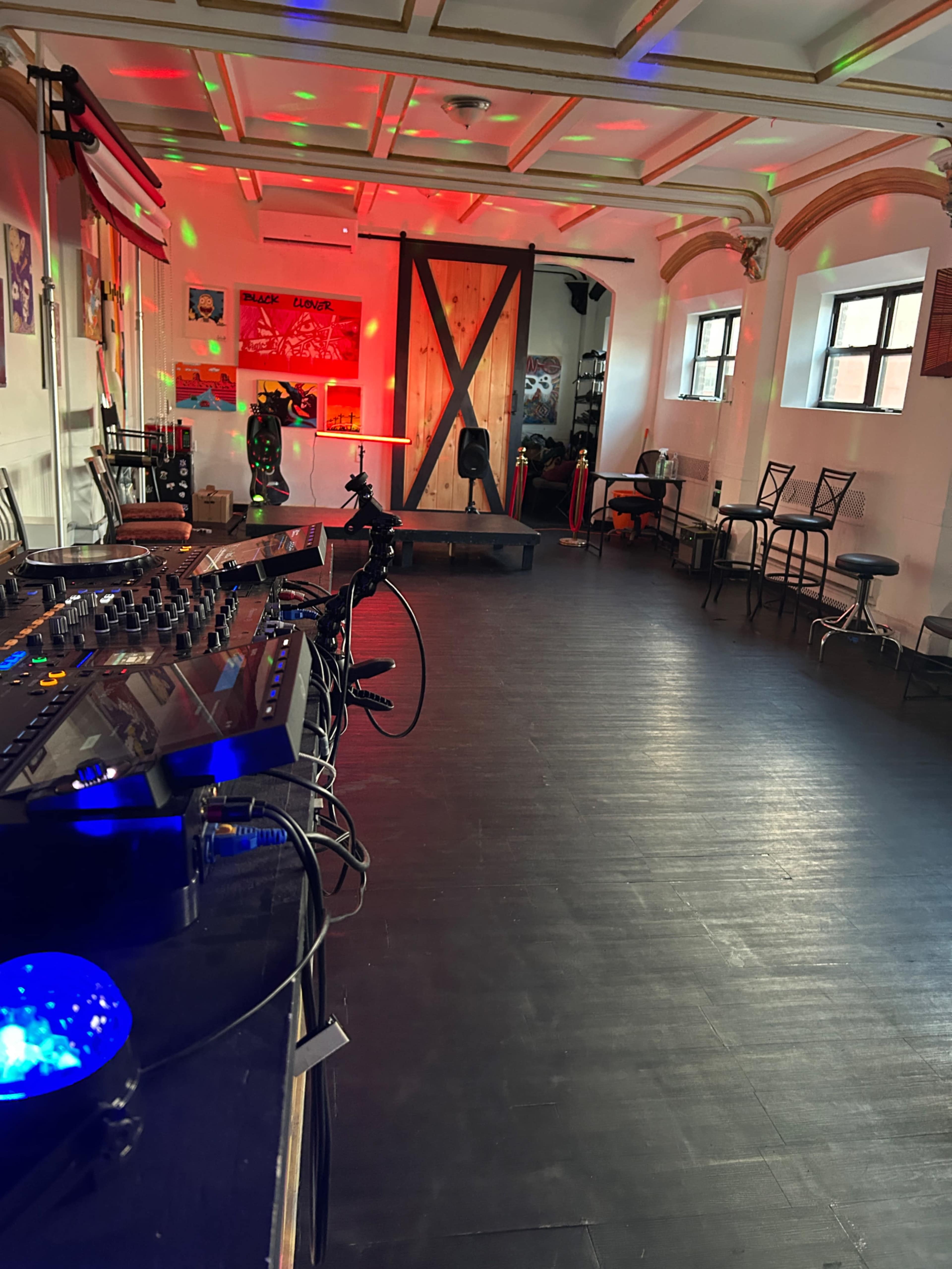 The image shows a spacious dance studio with colorful lights, a DJ setup on the left, and a wooden door at the back.