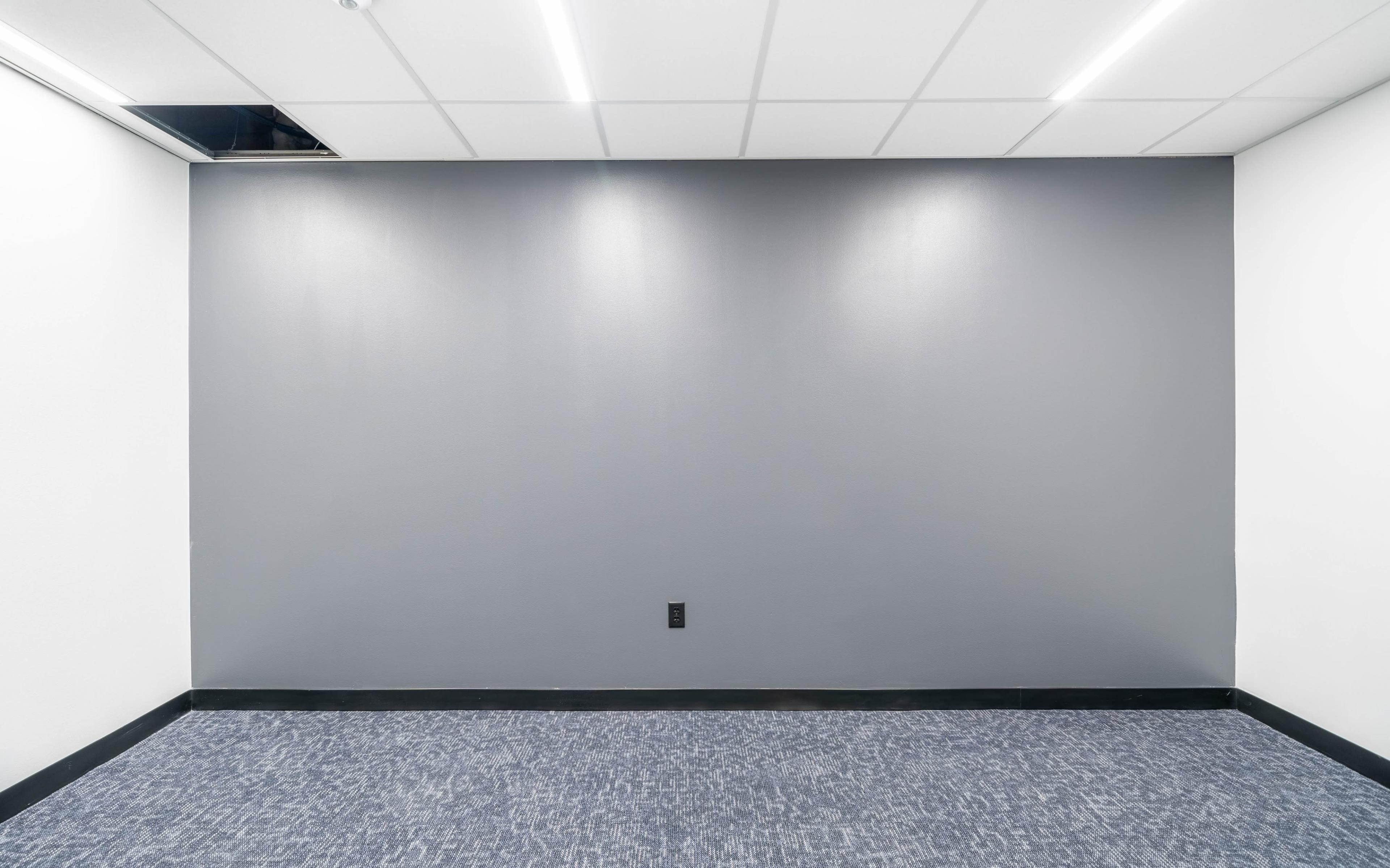 A sparsely furnished room with a gray wall, white ceiling, and carpeted floor.