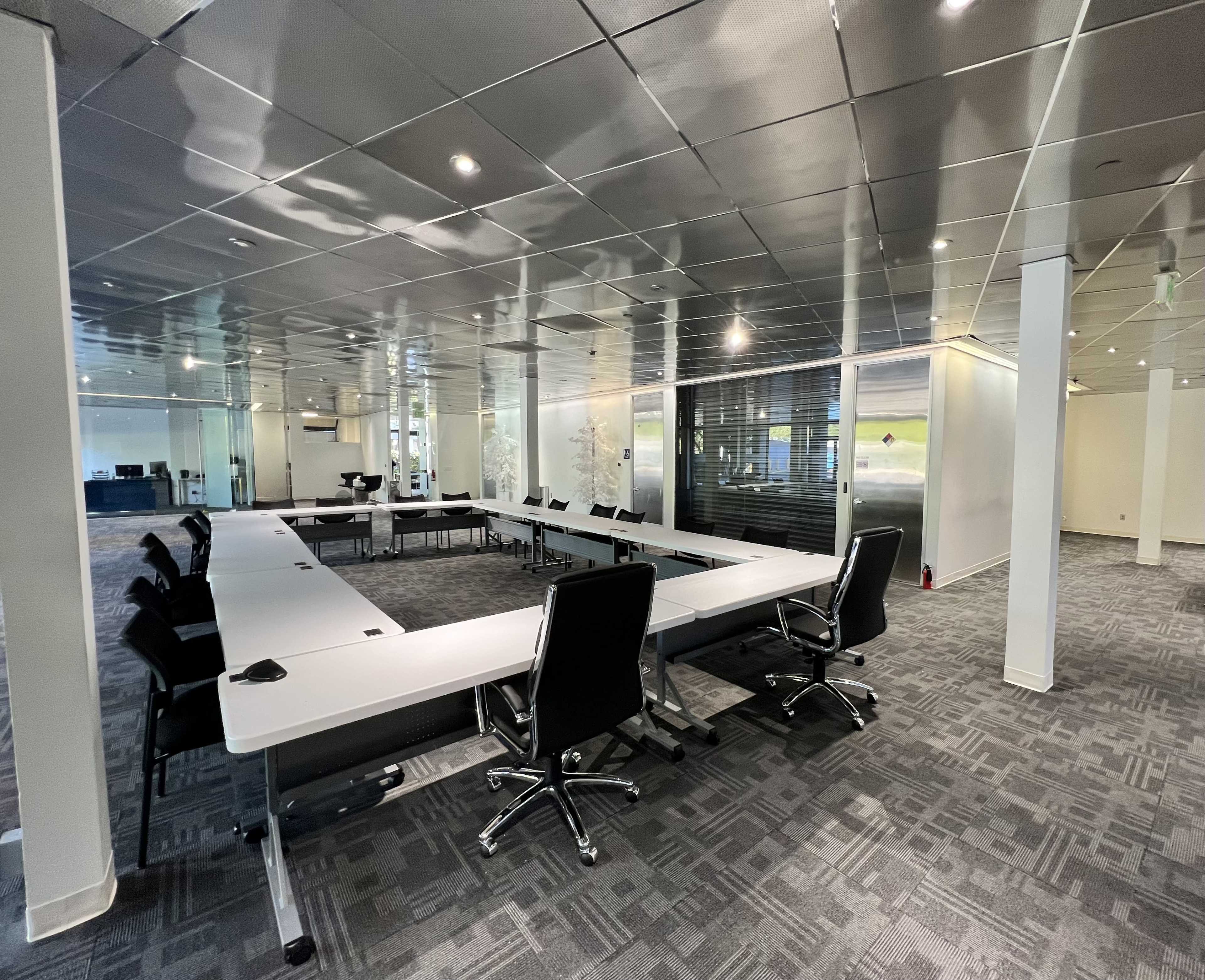 A modern conference room with a large rectangular table surrounded by black swivel chairs, and glass walls allowing visibility to adjoining spaces.