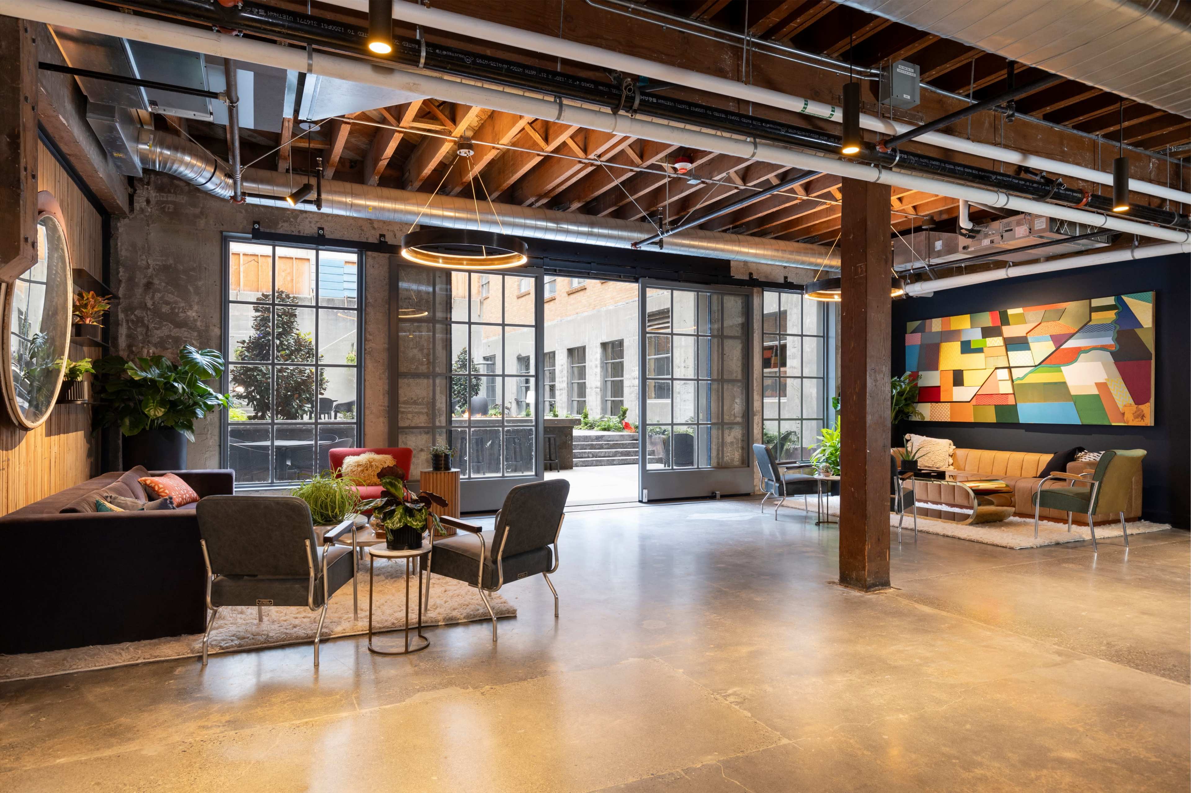 A modern lounge area with seating arrangements, large windows, and a colorful abstract wall mural.
