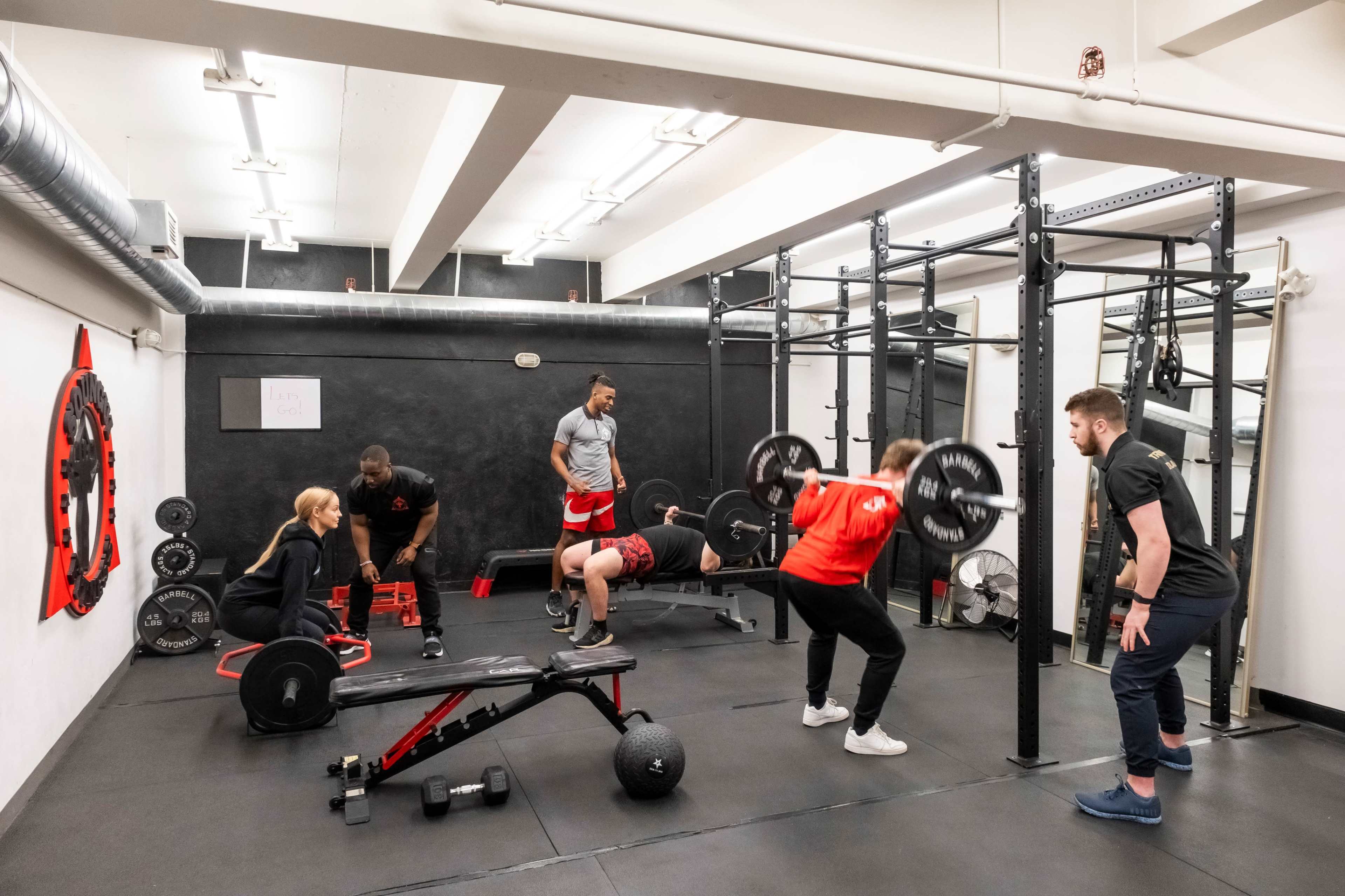 A group of individuals is engaged in various weightlifting exercises in a gym setting.